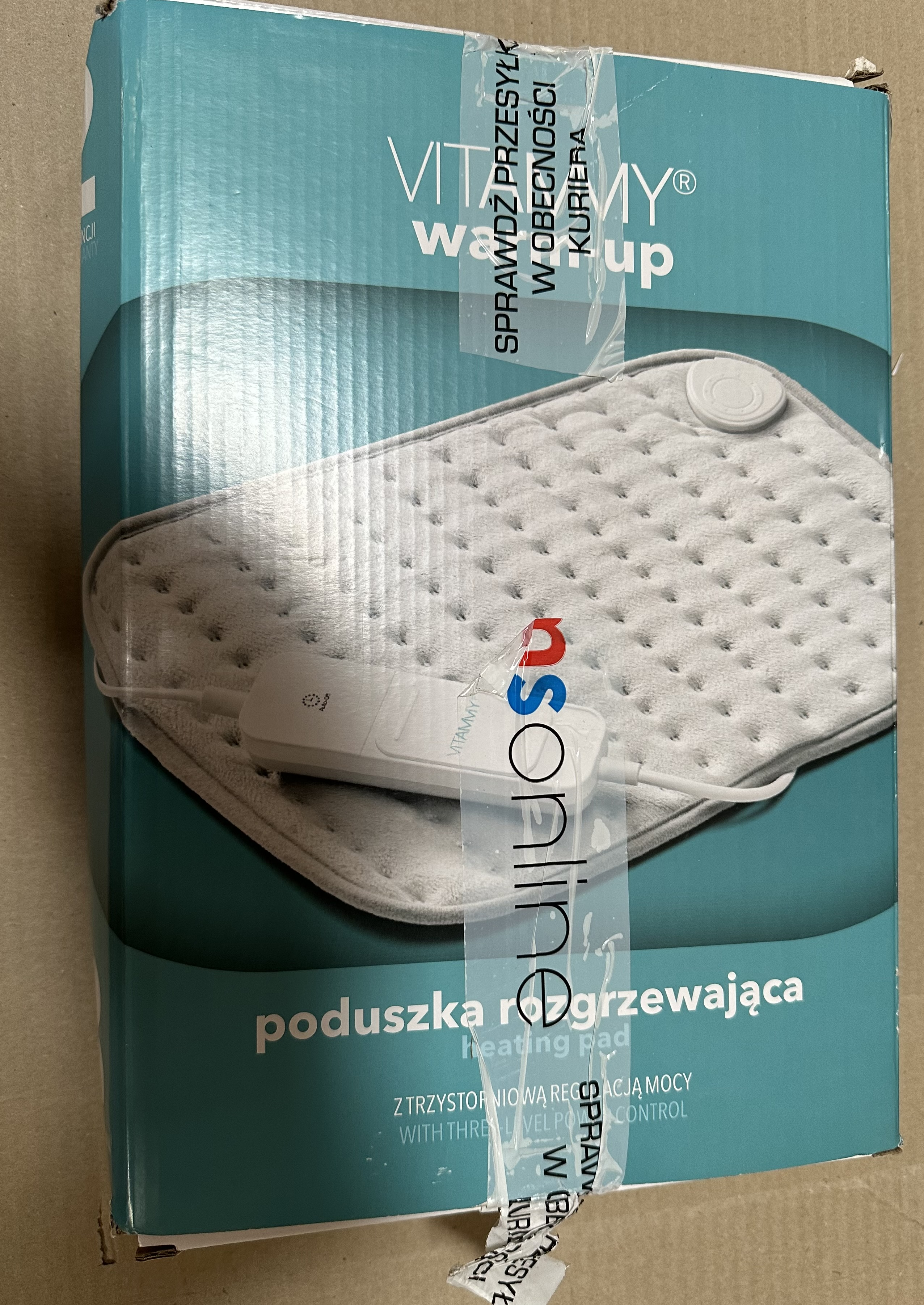 Poduszka rozgrzewająca w pudełku. Pudełko jest biało-niebieskie z tekstem w języku polskim. Z taśmą.