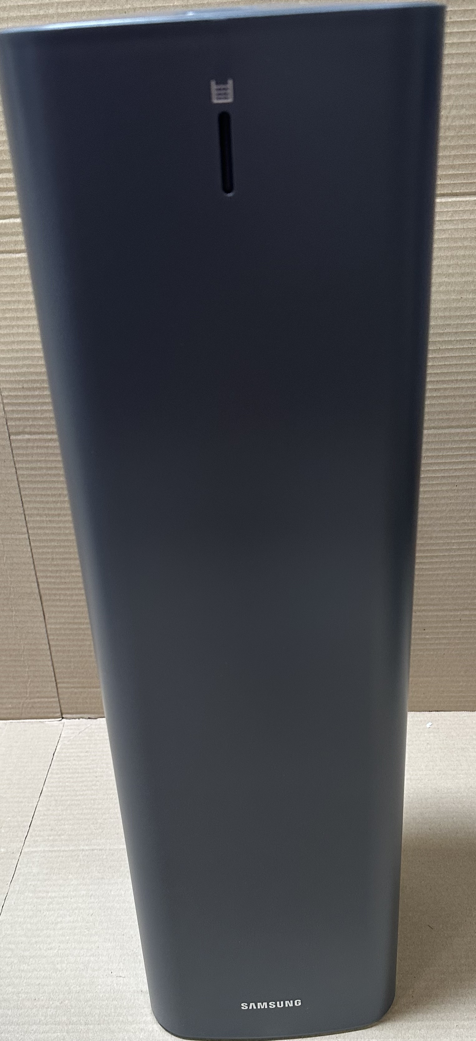 Ciemnoszary głośnik cylindryczny ze szczeliną i logo Samsung. Głośnik stoi na powierzchni.