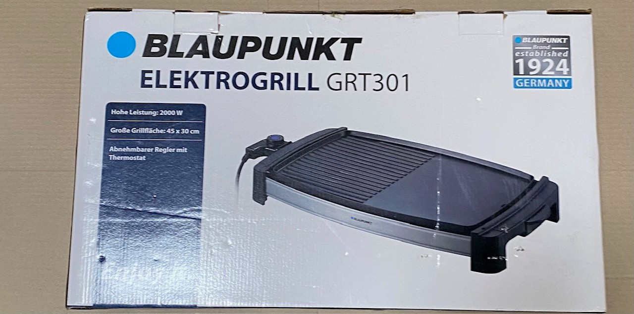 Zapakowany czarno-srebrny grill elektryczny Blaupunkt znajduje się na stole.