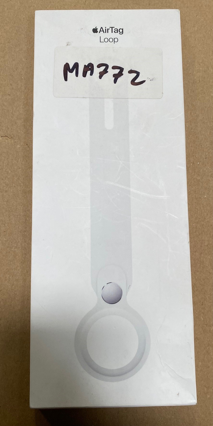 Białe pudełko Apple AirTag Loop z etykietą. Ręcznie pisana etykieta MA772.