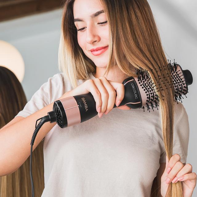 Kobieta szczotkuje włosy szczotką do kręcenia. Trzyma szczotkę do włosów w prawej ręce, a włosy w lewej.