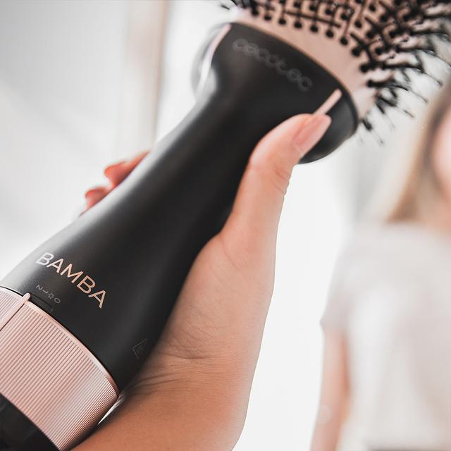 Dłoń trzymająca czarną i różowo-złotą suszarkę do włosów z napisem BAMBA.