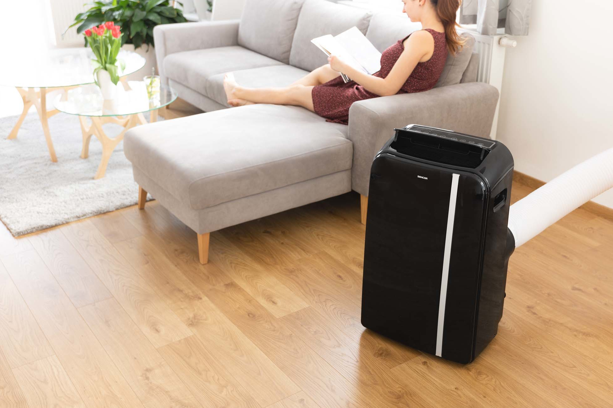 Kobieta czyta na sofie z czarnym klimatyzatorem i białym wężem.