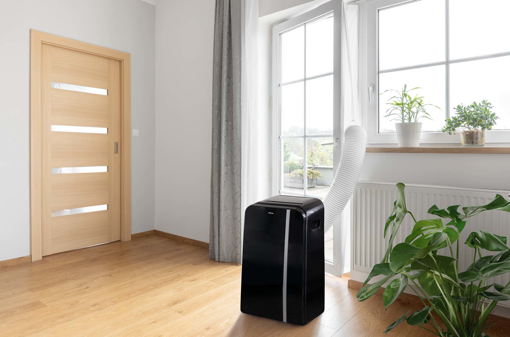 Czarny przenośny klimatyzator w pobliżu okna, z drzwiami w tle.