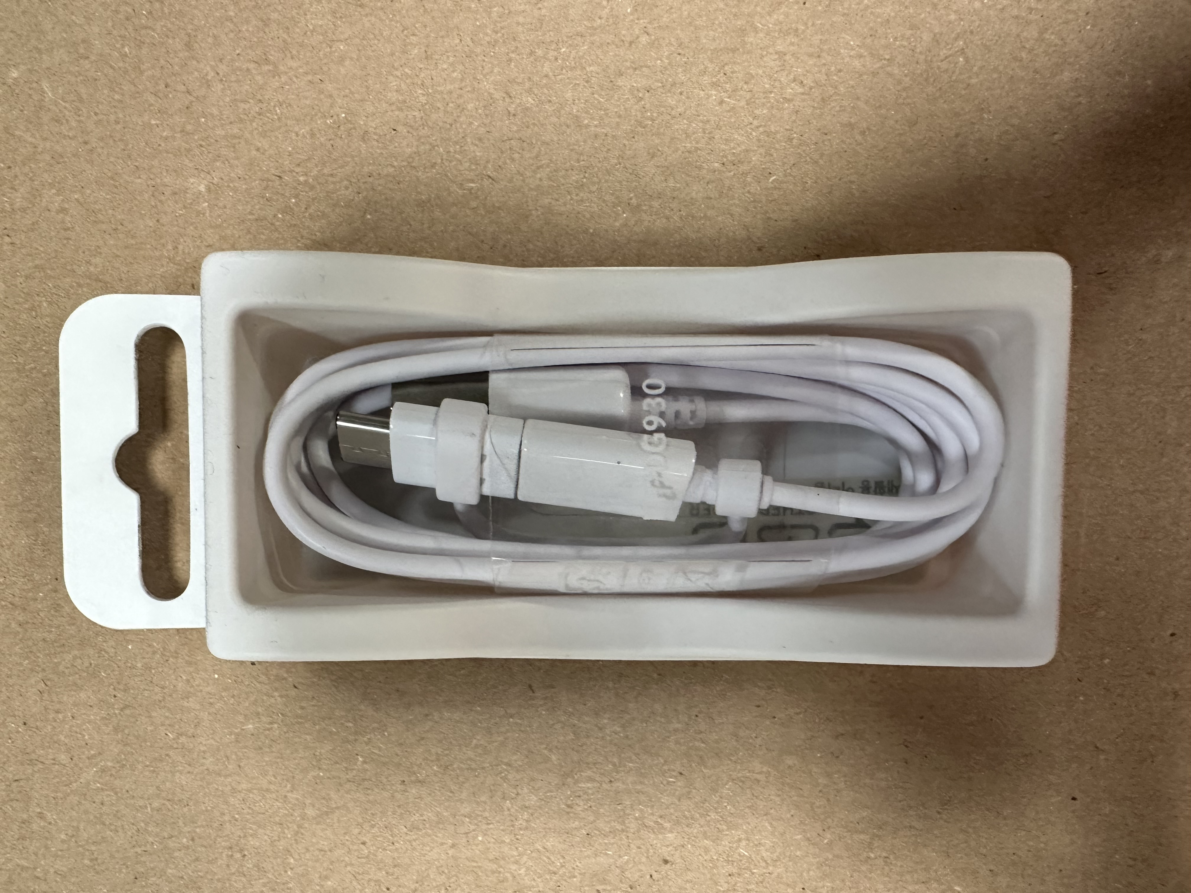 Biały kabel ładujący w białej plastikowej tacce, zdjęcie z góry.