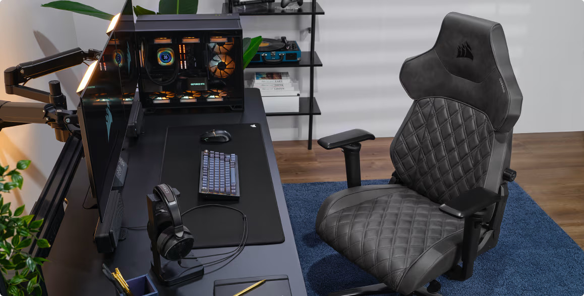 Konfiguracja do gier z czarnym biurkiem, krzesłem, monitorem i urządzeniami peryferyjnymi. Corsair jest na krześle.