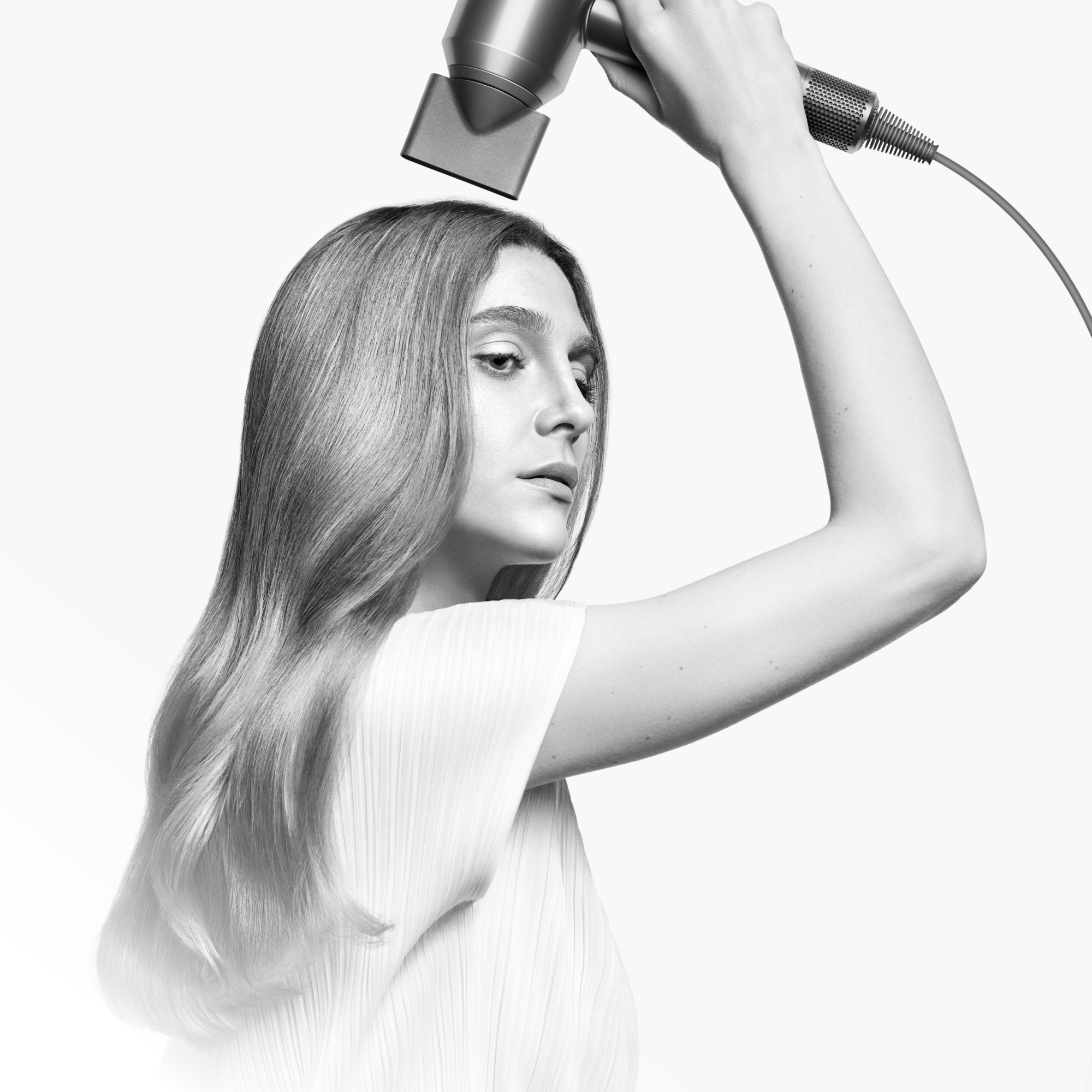 Mujer usando un secador de pelo Dyson plateado.