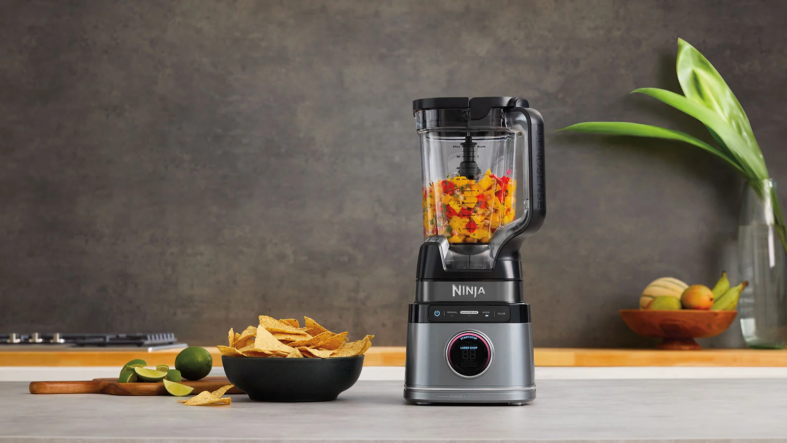 Turmixgép étellel, lime-okkal és egy tál chipsszel egy szürke pulton.