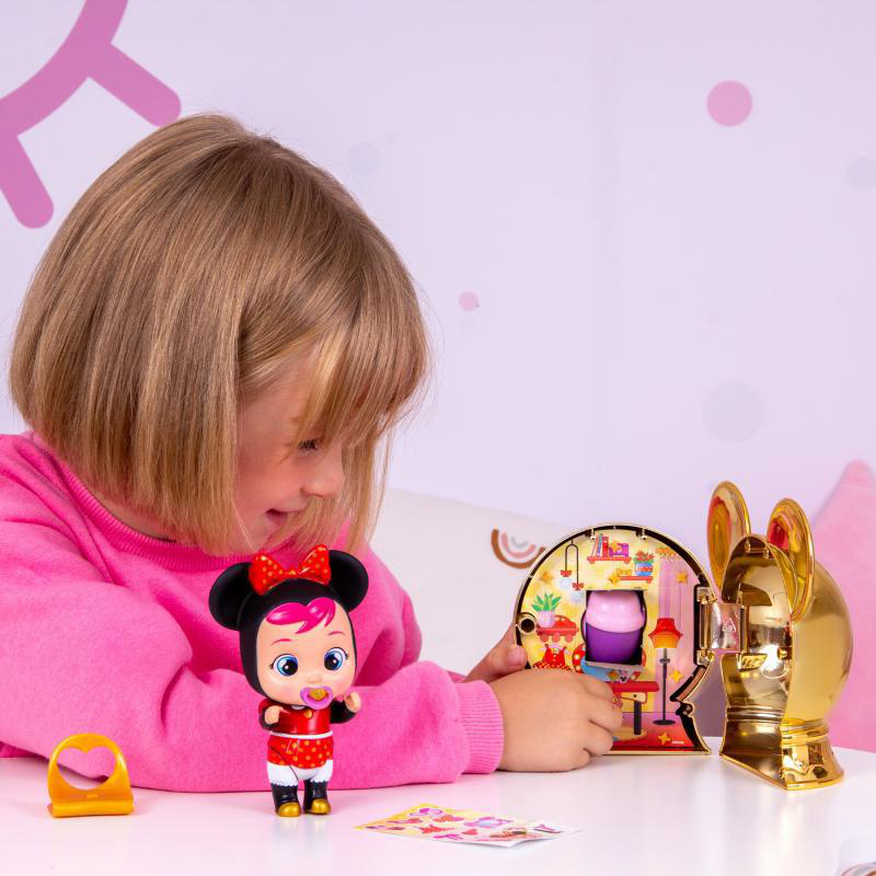 Ein Kind spielt mit Spielzeug auf einem weißen Tisch. Es gibt eine Puppe, einen goldenen Hasenkopf und ein kleines Spielzeughaus.