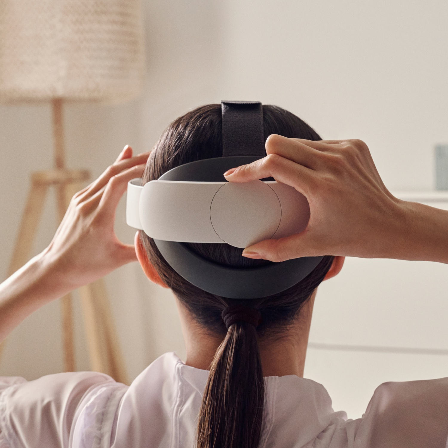Una donna indossa un visore VR, mani che lo regolano. Lo sfondo è sfocato.