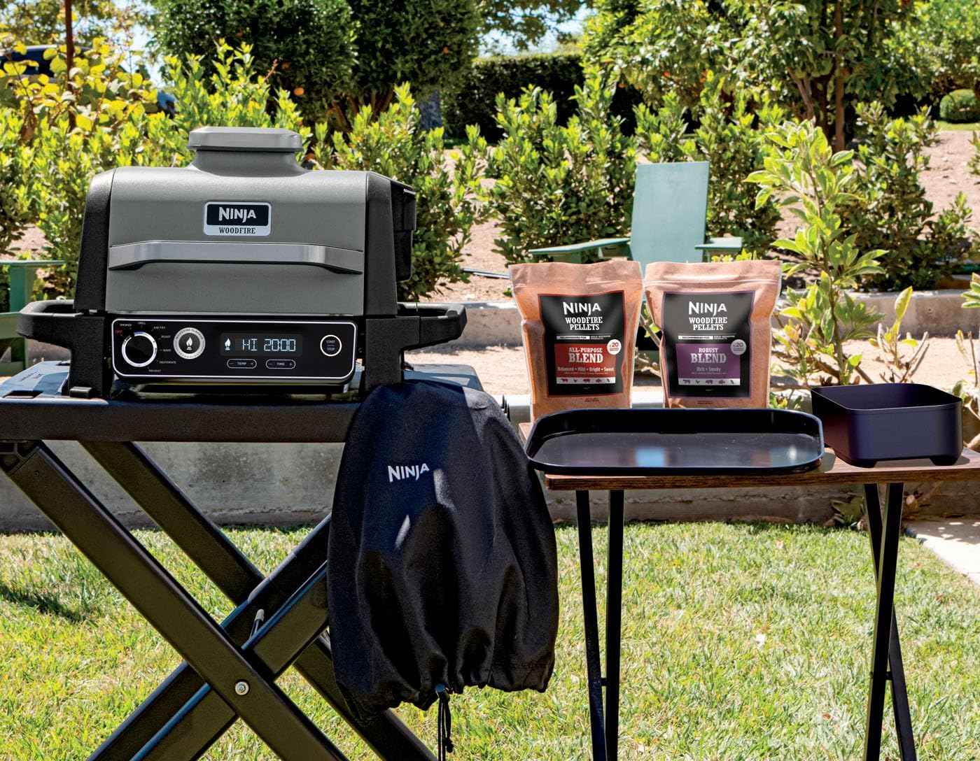 Ninja Woodfire grill egy asztalon, kiegészítőkkel, napos kertben.