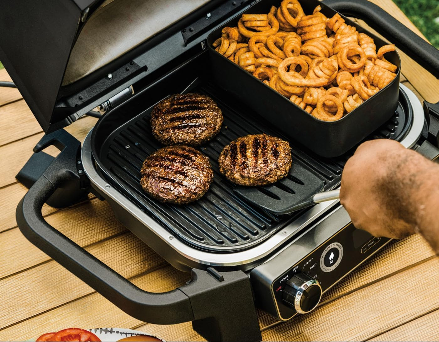 Grill hamburgerekkel és sült krumplival. Egy személy egy spatulával fordít meg egy hamburgert.