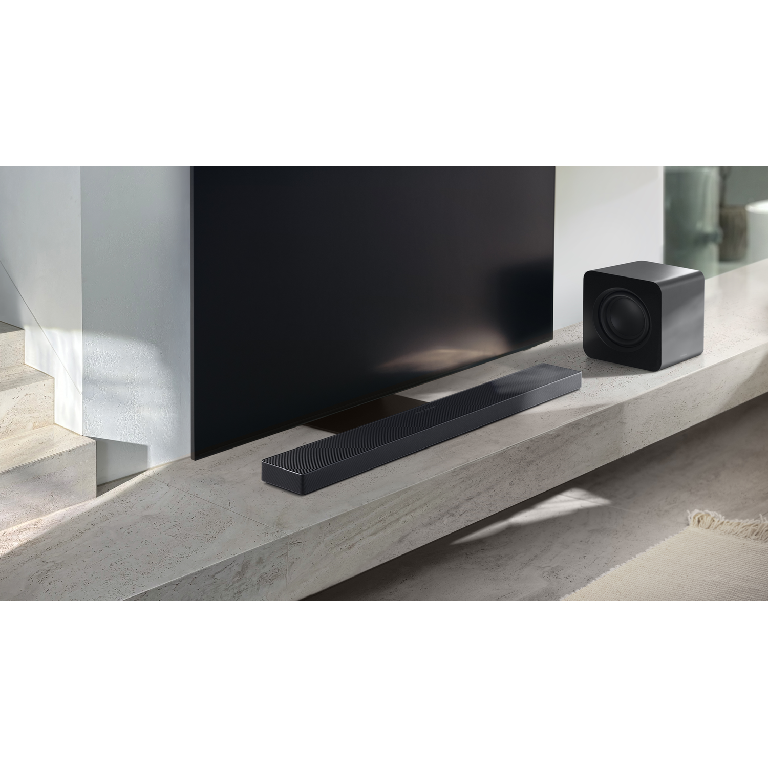 A black soundbar and subwoofer on a marble shelf in front of a TV.