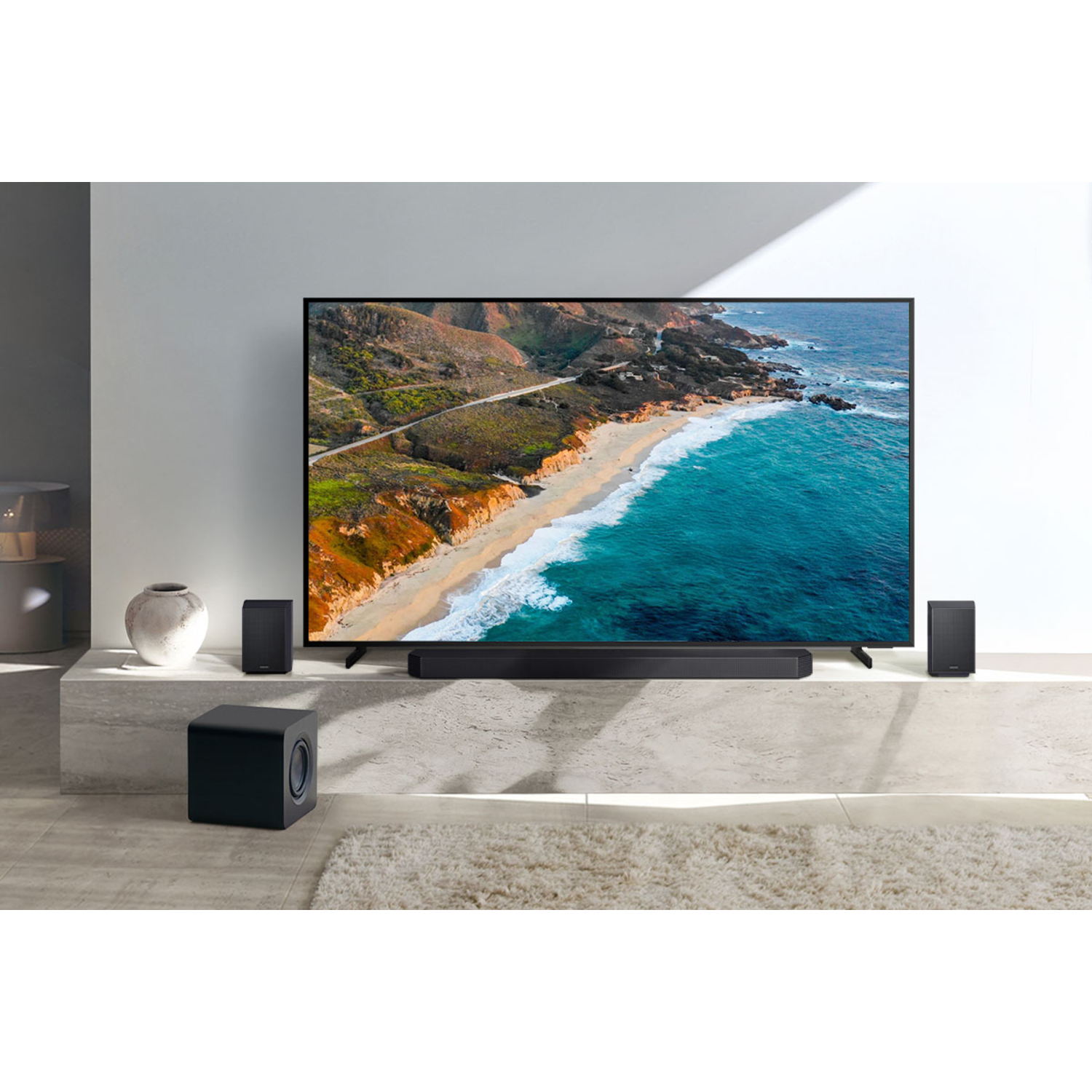 Een tv toont een strandscène. Luidsprekers en subwoofer vooraan. De kamer is modern en helder.