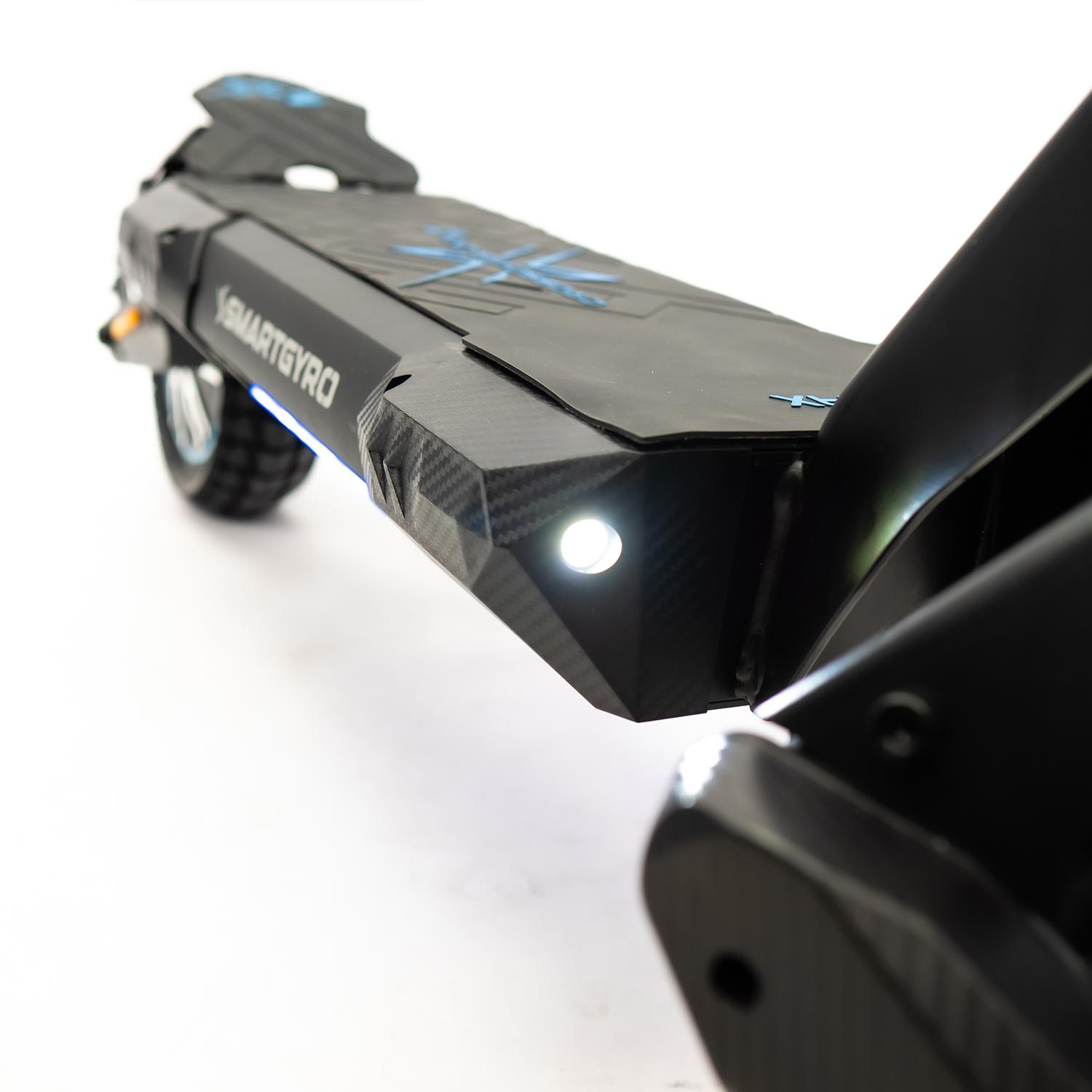 Patinete eléctrico negro, vista frontal. Tiene un faro encendido y detalles azules.