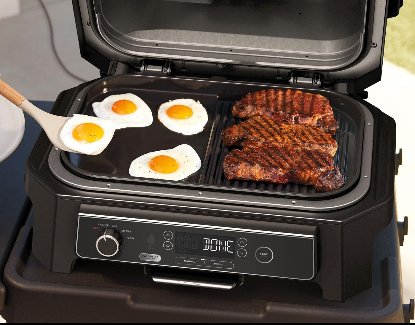 Egy grill tojással és steakkel. Egy személy spatulát használ.