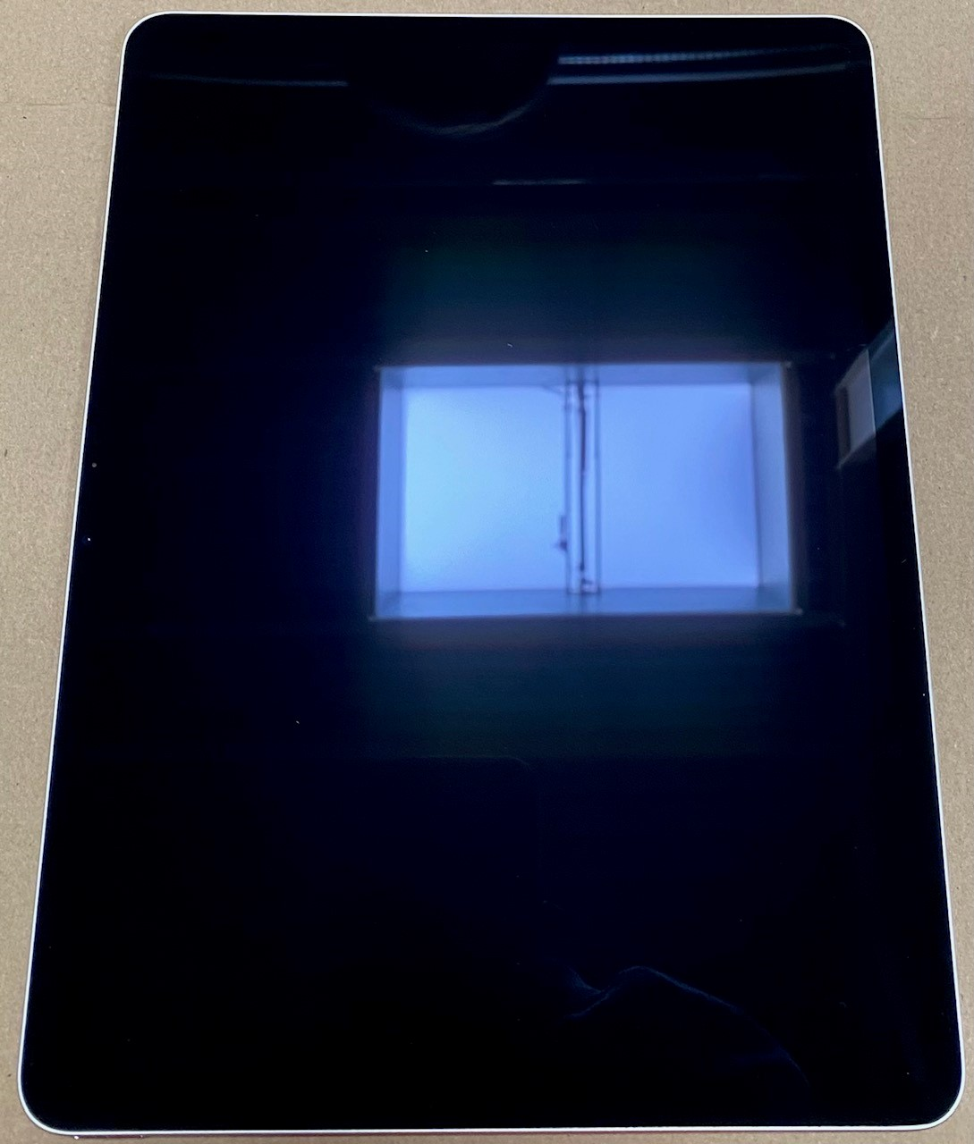 Ekran tabletu, czarny, pokazujący odbicie okna.  Tablet ma jasną ramkę.