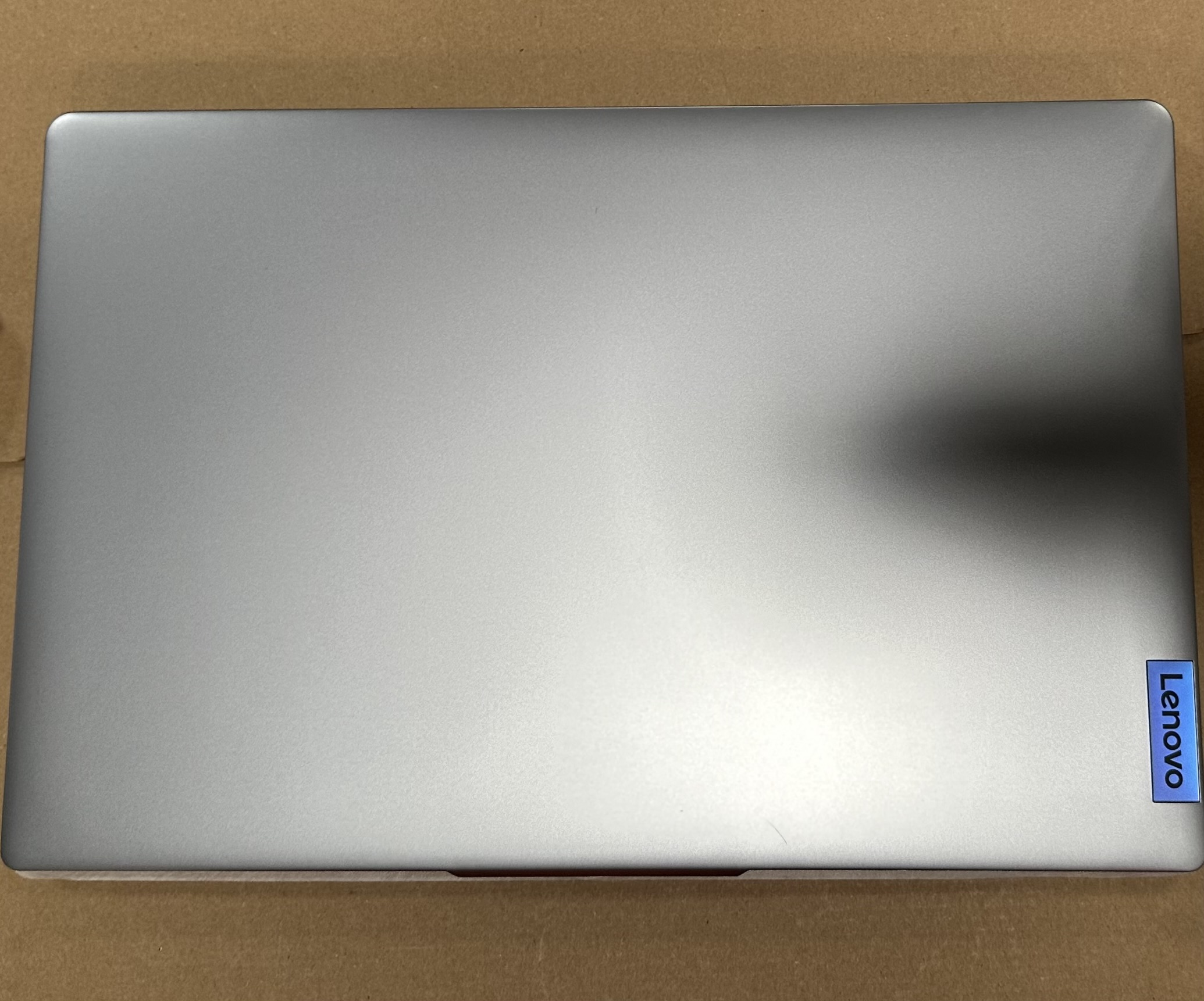 Srebrny laptop jest zamknięty, pokazując logo Lenovo na pokrywie.