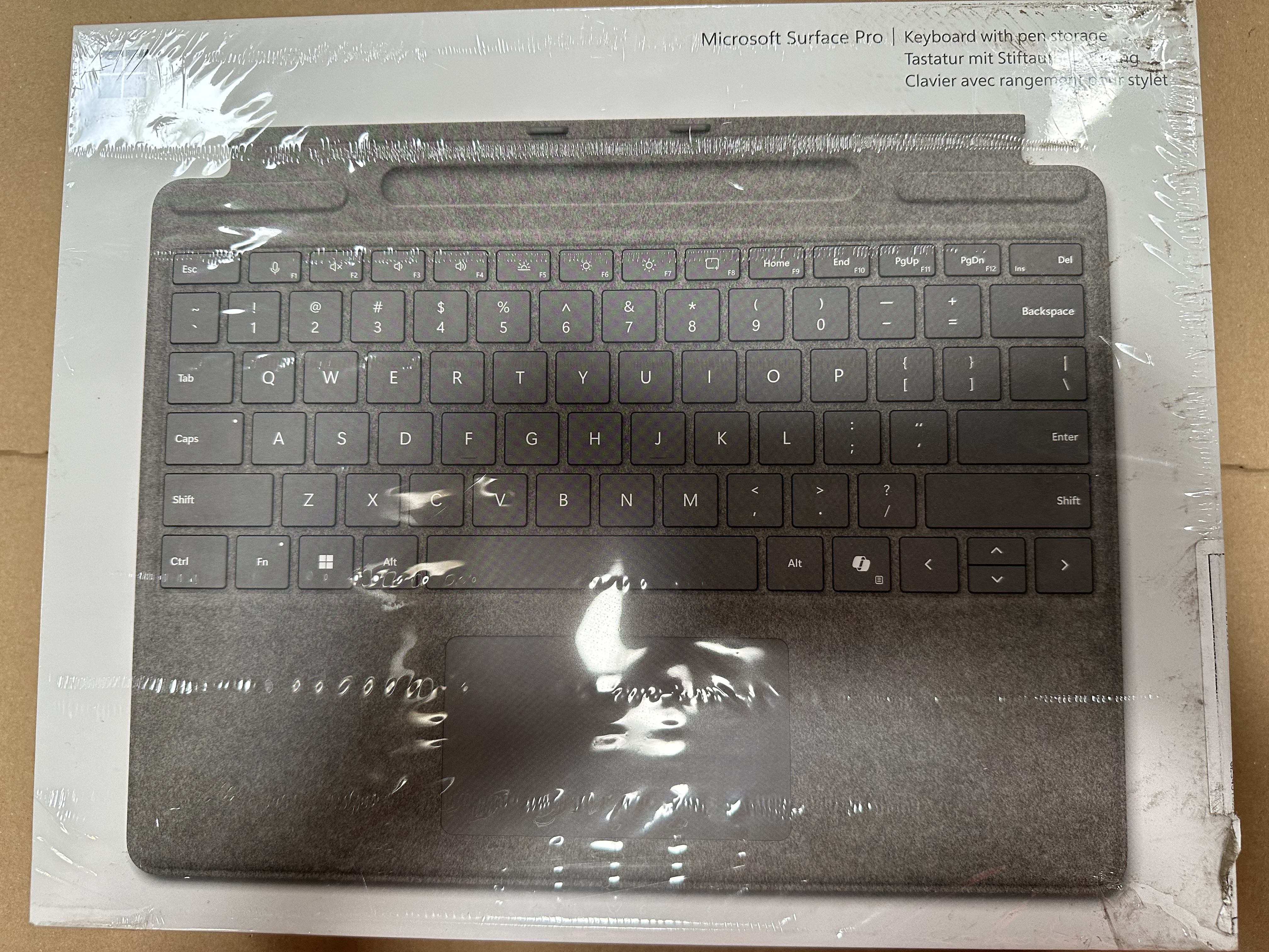 Klawiatura z panelem dotykowym w plastikowym opakowaniu, z etykietą Microsoft Surface Pro.