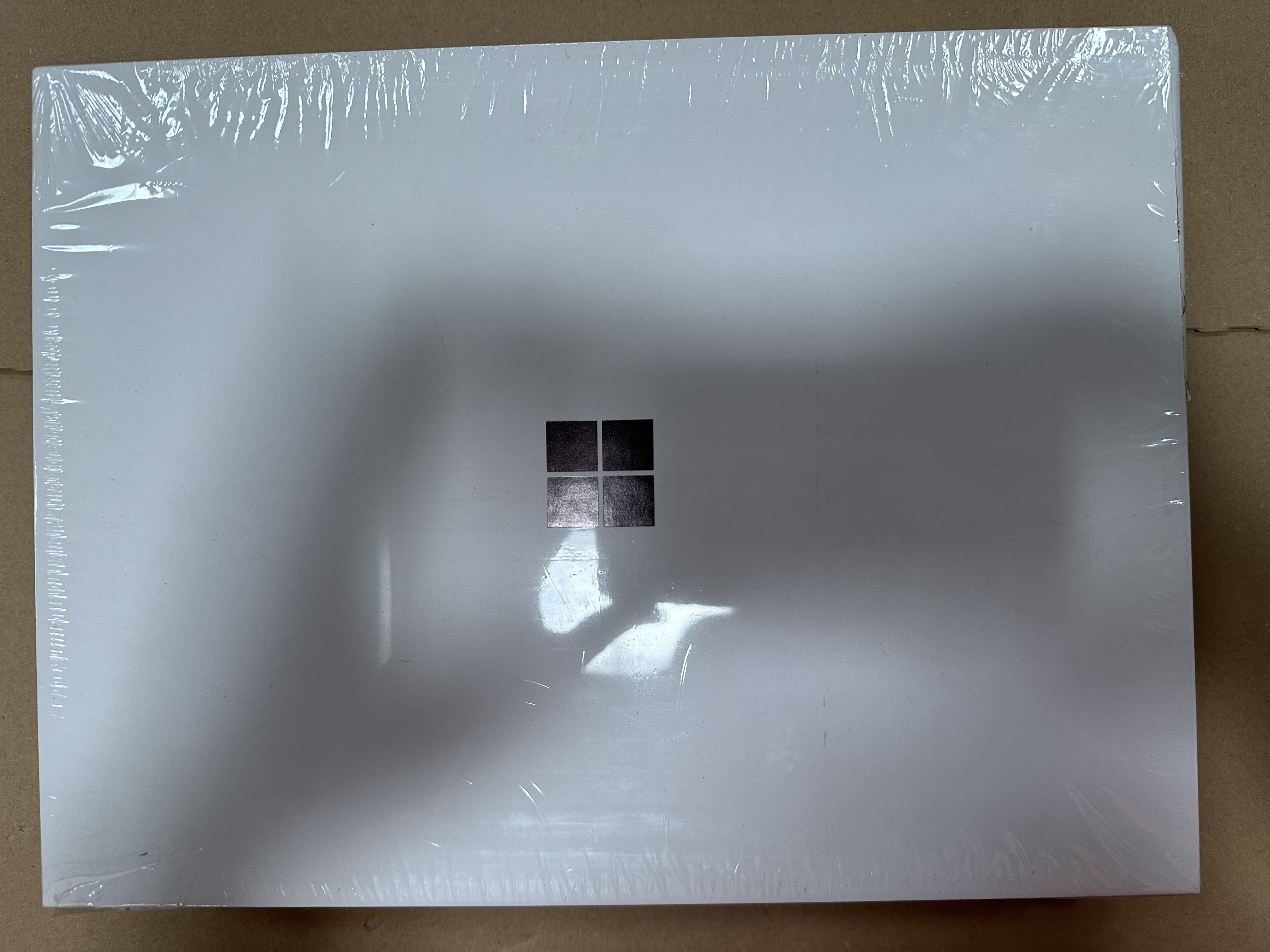 Biały laptop zamknięty, zapakowany w plastik.