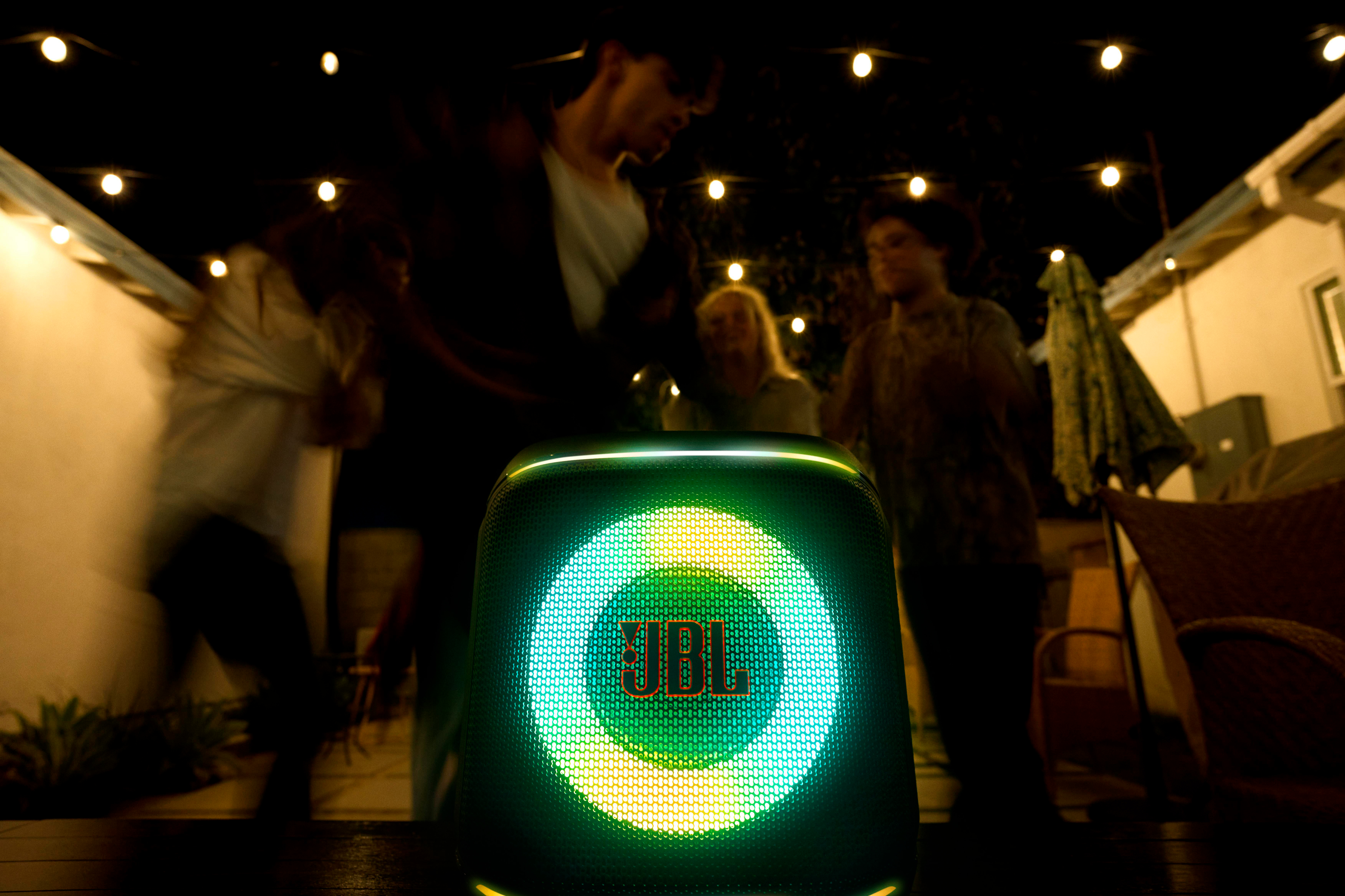 Tanzende Menschen in der Nähe eines beleuchteten JBL-Lautsprechers bei Nacht.