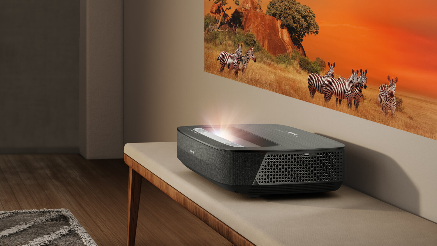 Projektor na ławce wyświetlający obraz zebr o zachodzie słońca na ścianie.