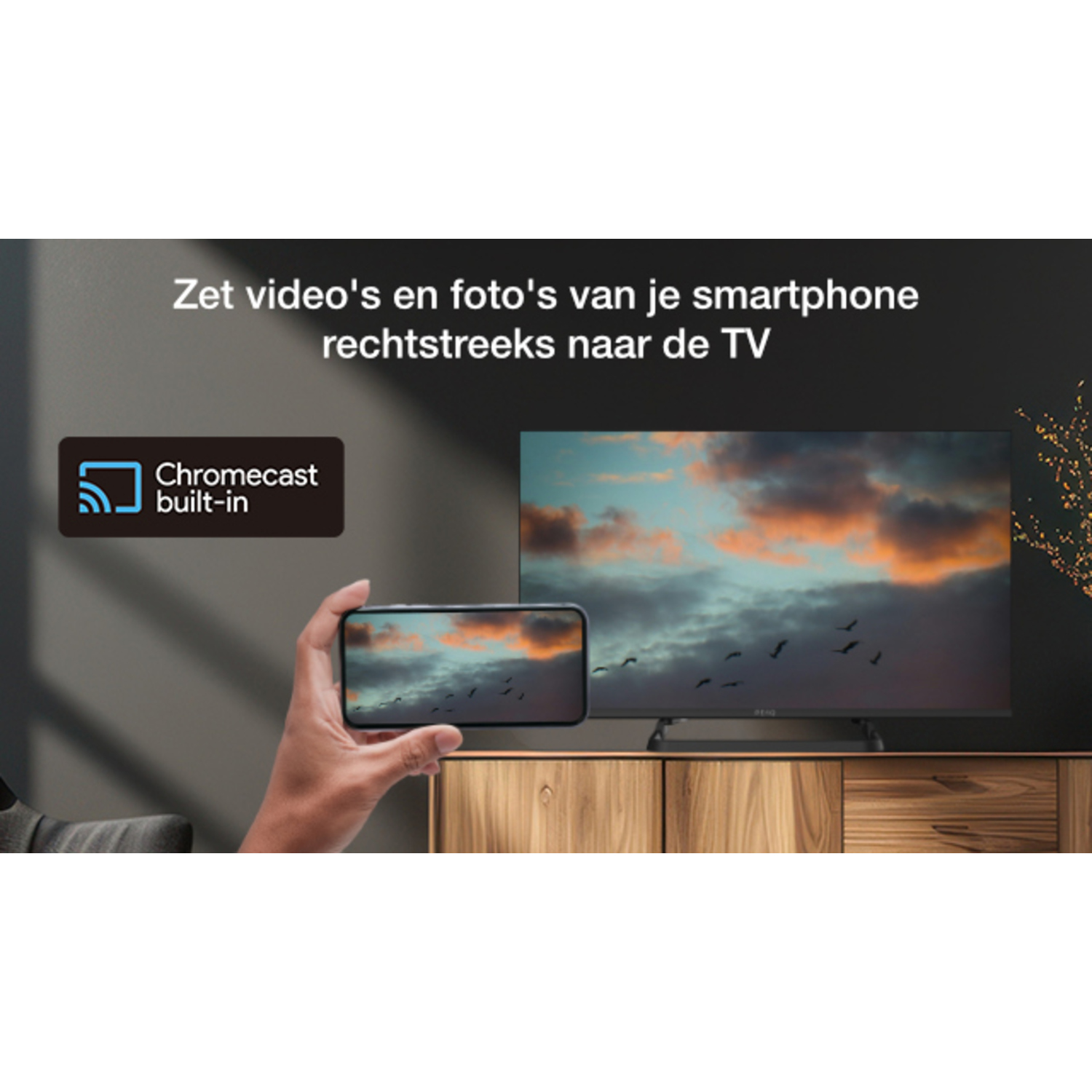 TV screen showing a sunset over the ocean. A hand holding a phone casts the image.