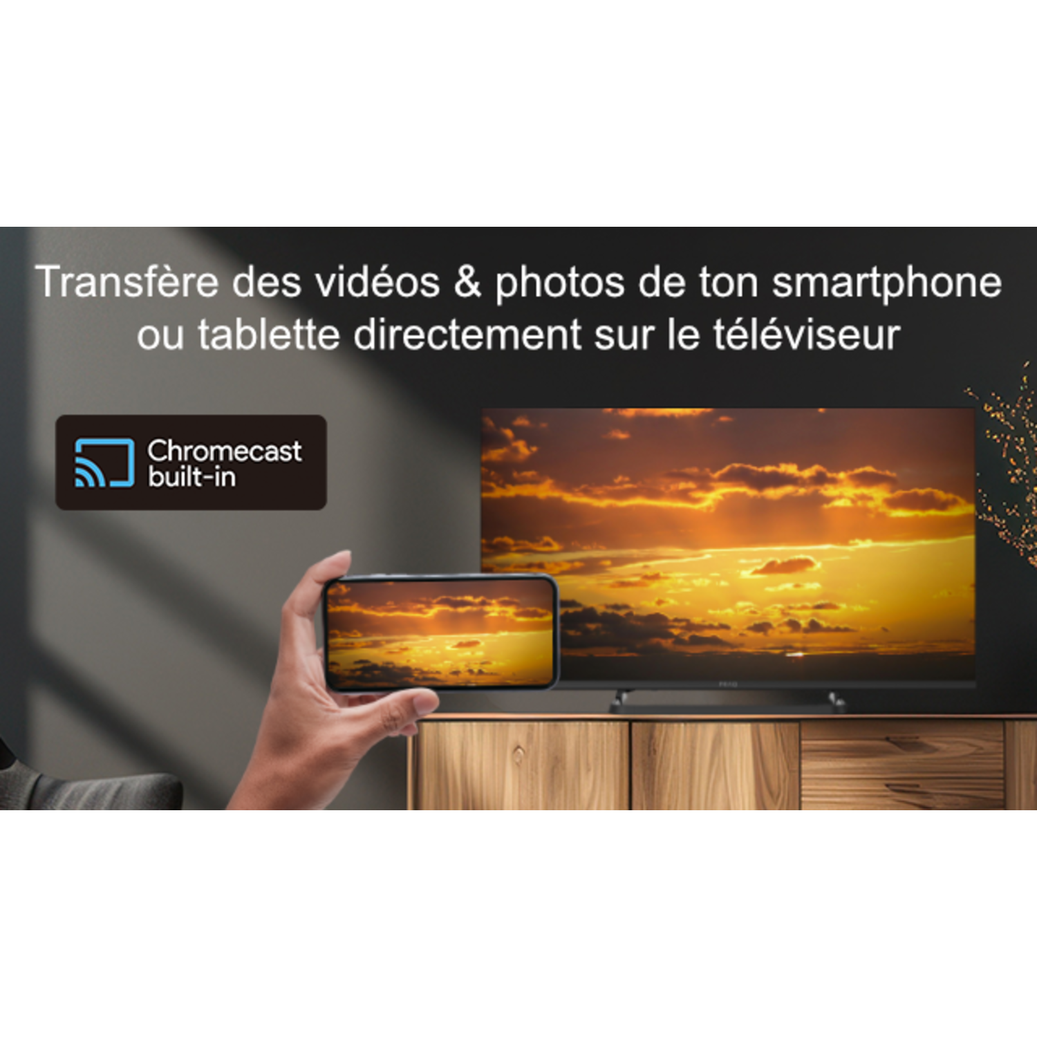 Une main tenant un téléphone montre un coucher de soleil sur un écran de télévision.