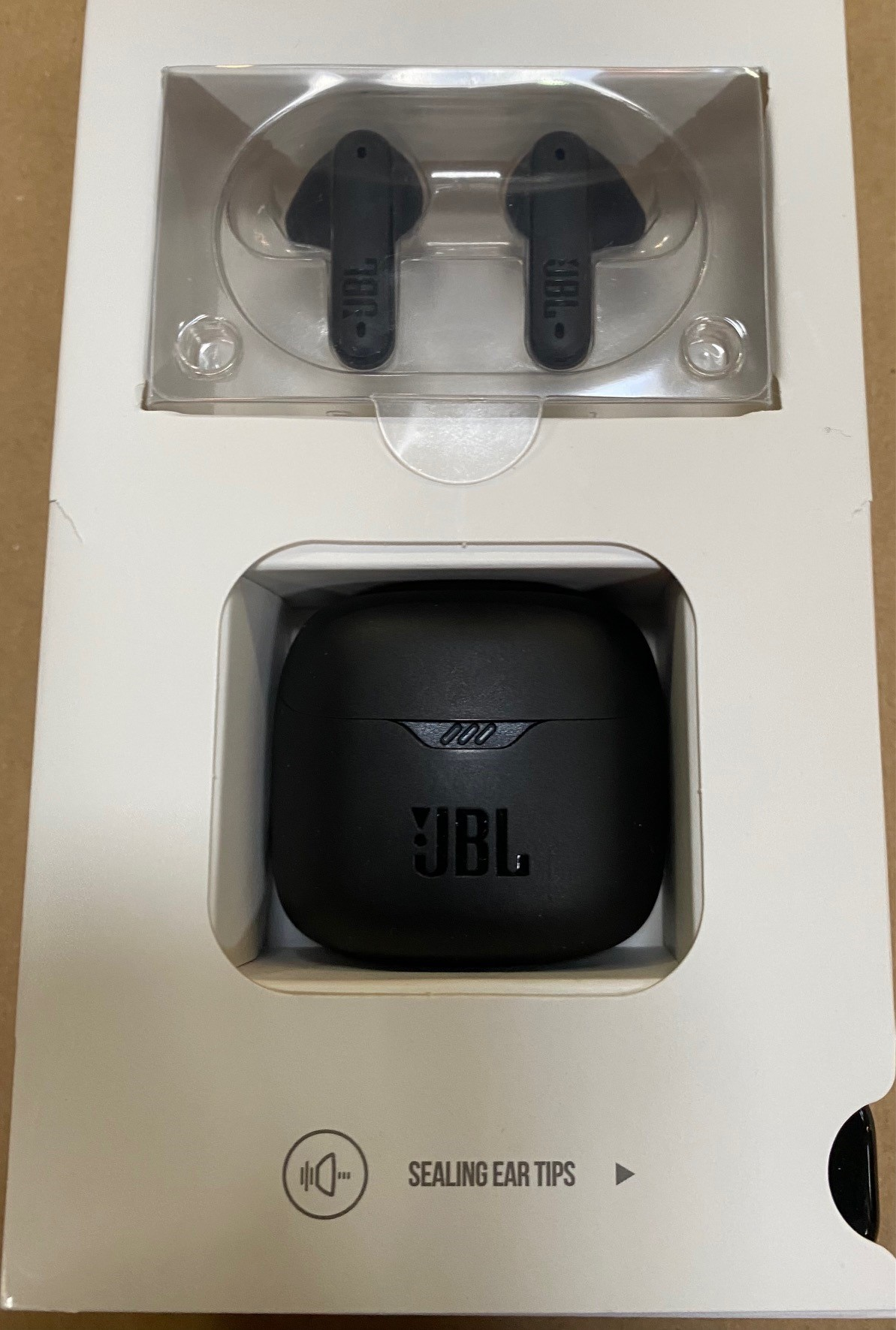 Czarne etui z czarnymi słuchawkami JBL. Etui znajduje się w białym pudełku.