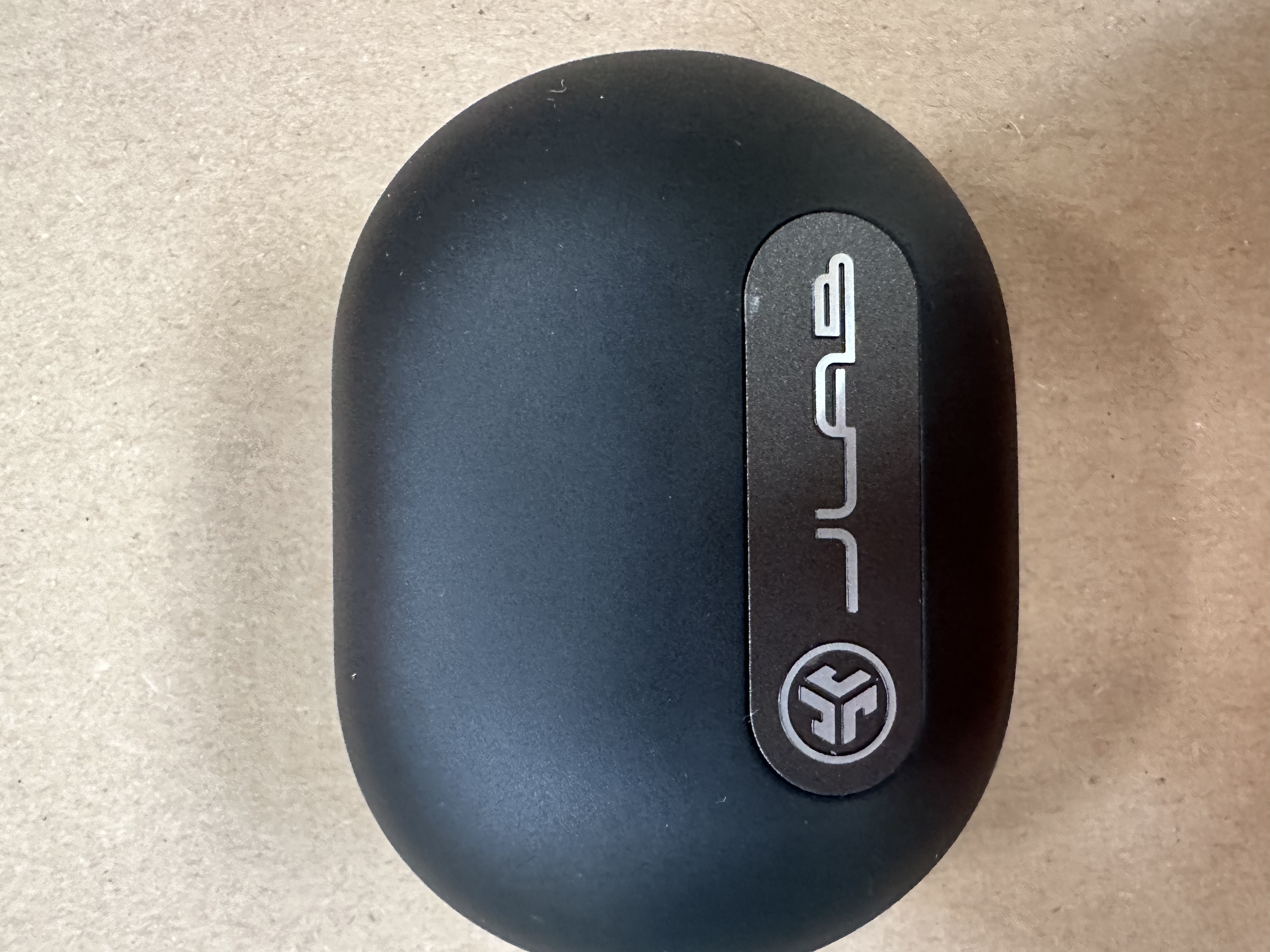 Czarne, owalne etui ładujące ze srebrnym logo na jasnobrązowej powierzchni.