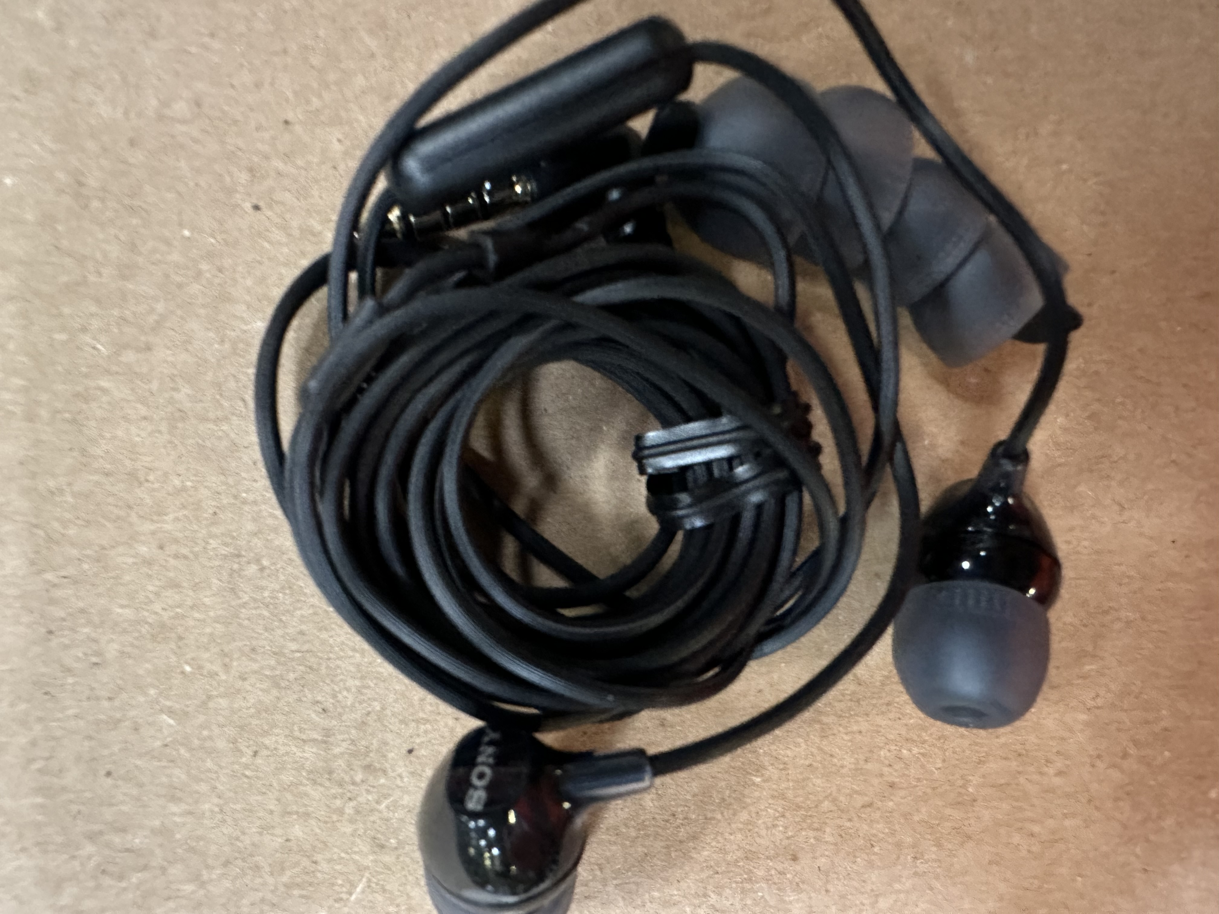 Poplątana wiązka czarnych słuchawek z modułem sterującym. Umieszczone na drewnianej powierzchni.