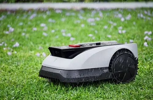 Kosiarka robotyczna na trawie, z kroplami deszczu i rozmytym tłem.
