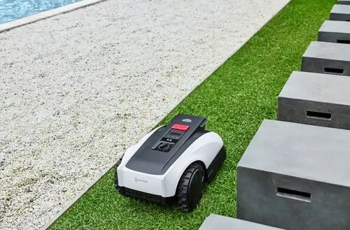Kosiarka robotyczna na zielonej trawie obok kamiennej ścieżki.