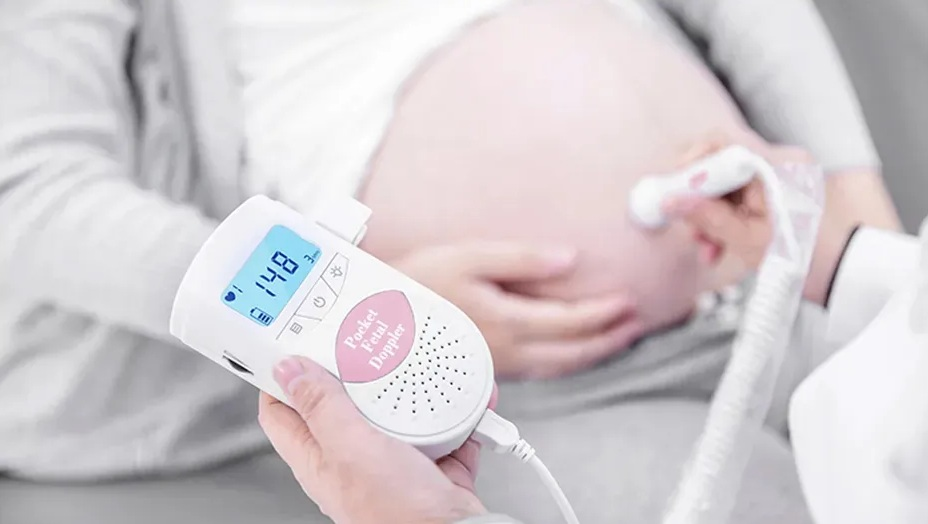 Brzuch ciężarnej kobiety jest badany za pomocą kieszonkowego Dopplera płodowego. Urządzenie jest białe.
