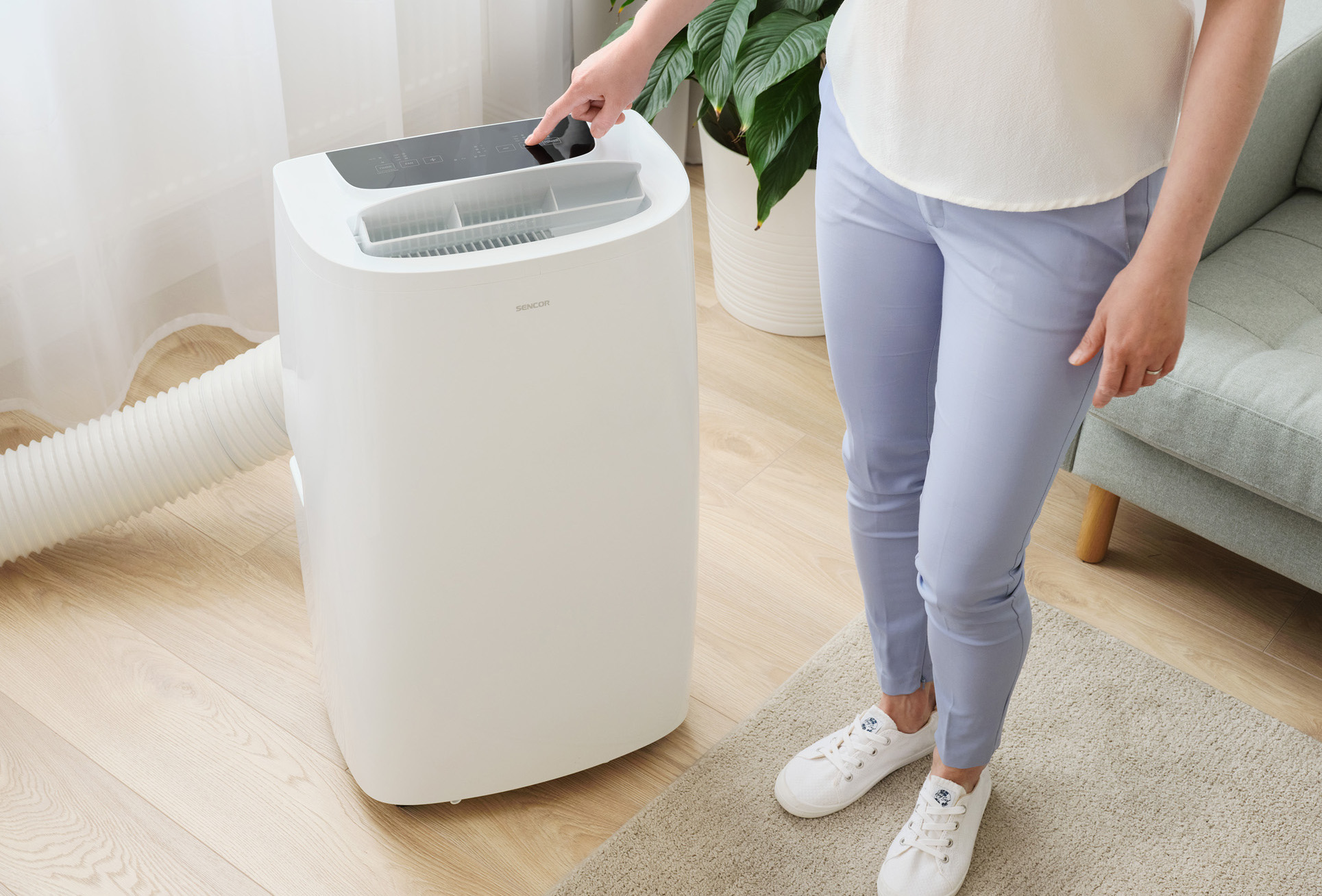 Kobieta obsługująca białą przenośną klimatyzację, stojąca w pokoju.