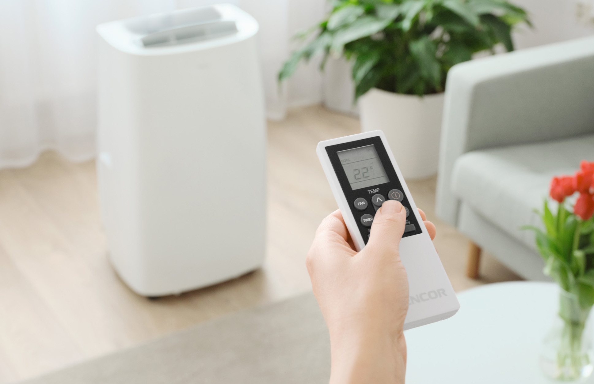 Biała chłodziarka powietrza z ręką używającą pilota, ustawiająca temperaturę.