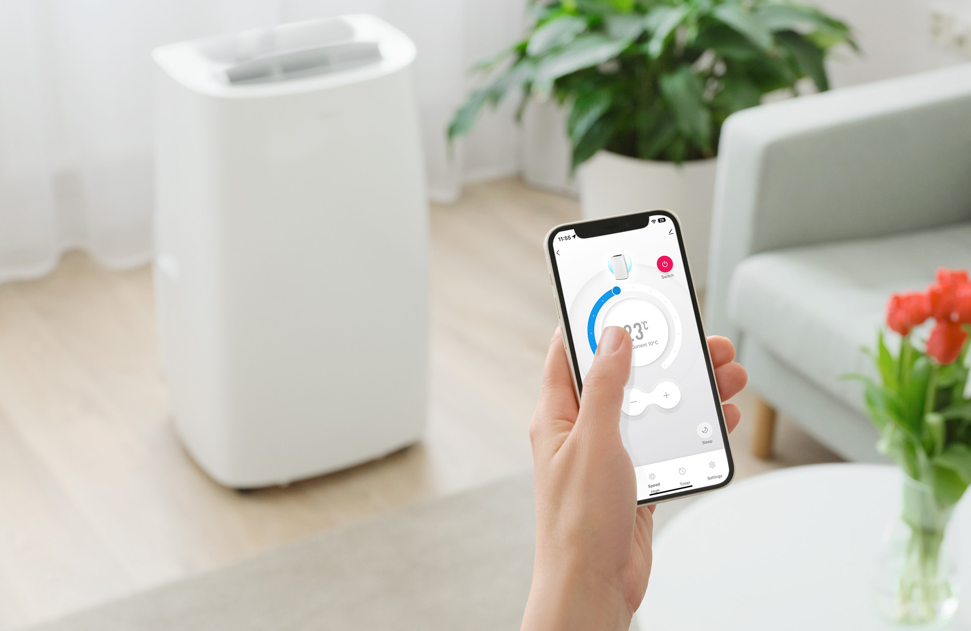 Dłoń trzymająca smartfon z panelem sterowania, przed białą oczyszczaczem powietrza.