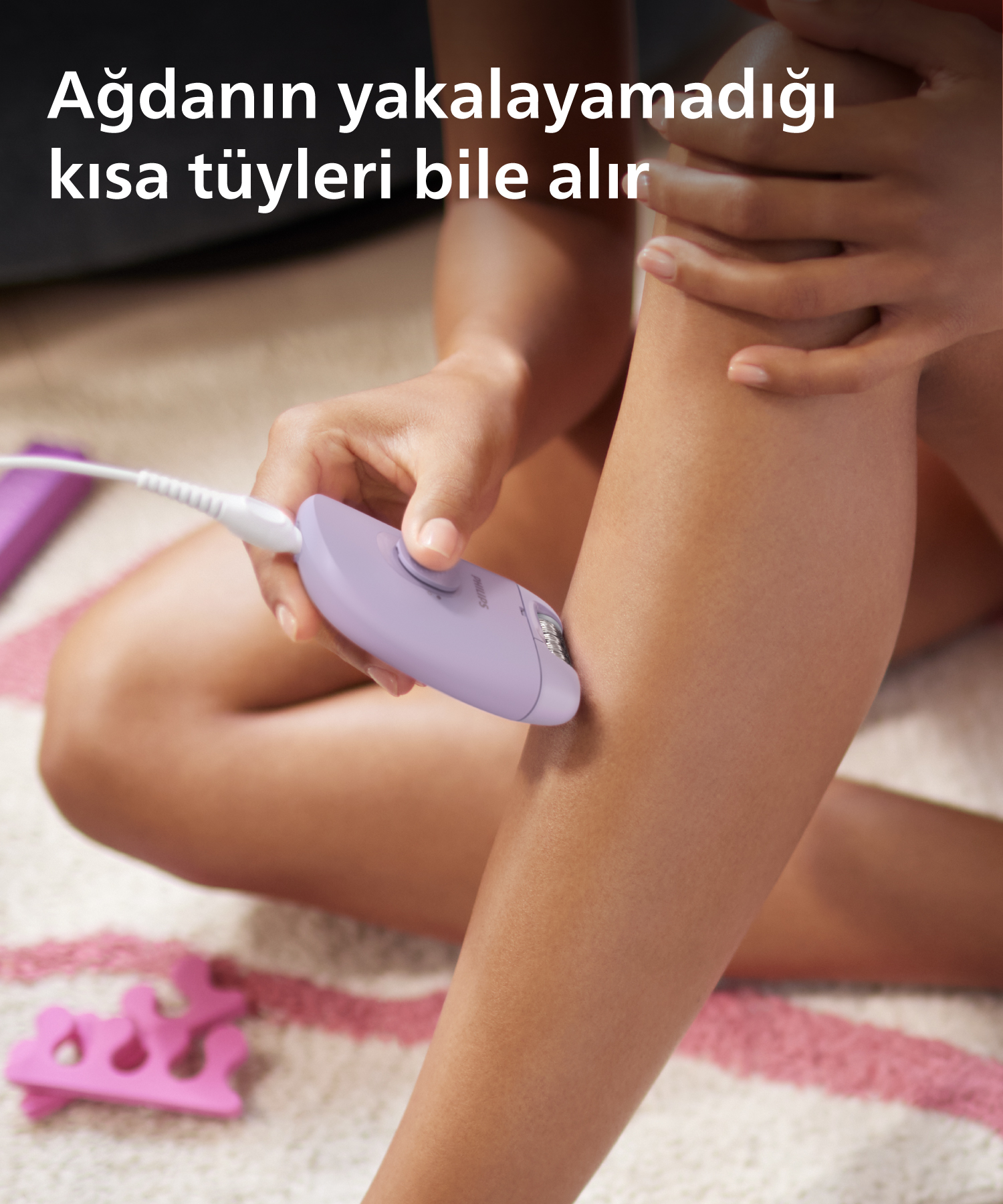 Bacağında epilatör kullanan kadın. Cihaz mor renktedir. Metin: Kısa tüyleri bile alır.