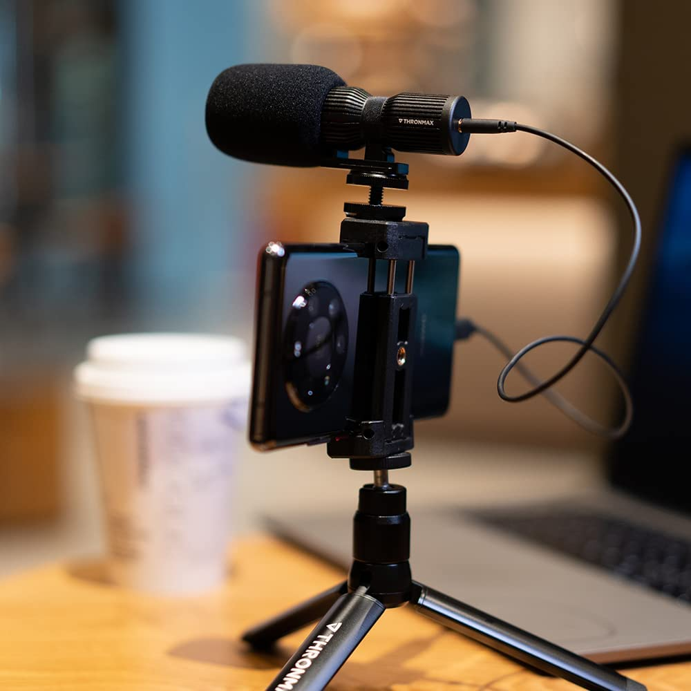 Bir tripod üzerine sabitlenmiş bir telefonda bir mikrofon. Kahve fincanı ve dizüstü bilgisayar görülebilir.