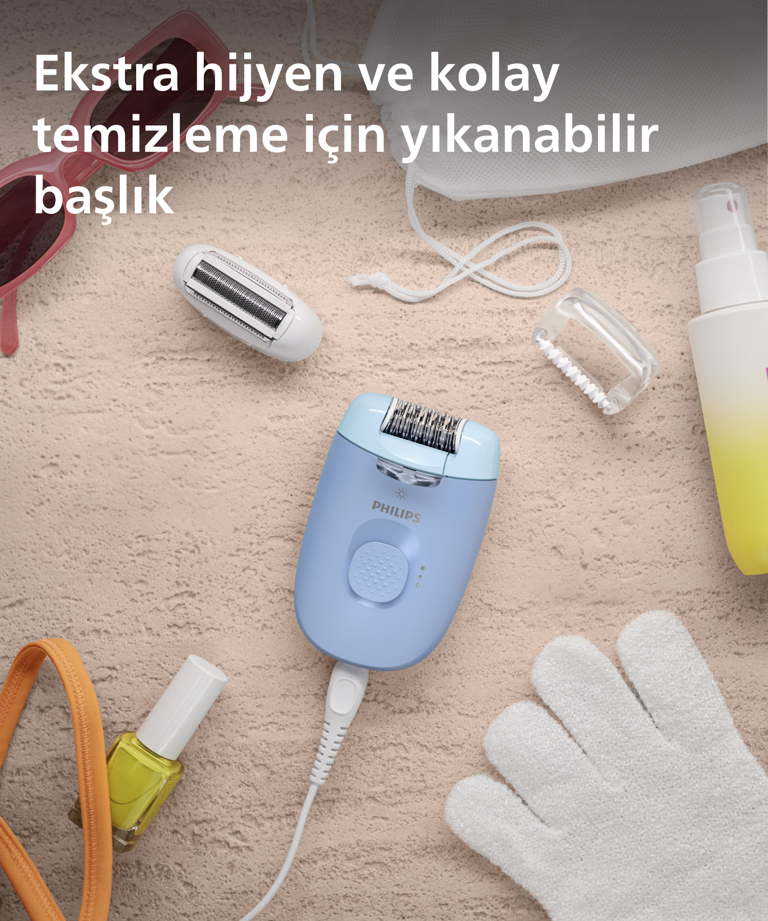 Mavi epilatör, kumlu yüzeyde aksesuarlarla. Güneş gözlüğü ve beyaz bir çanta da mevcut.