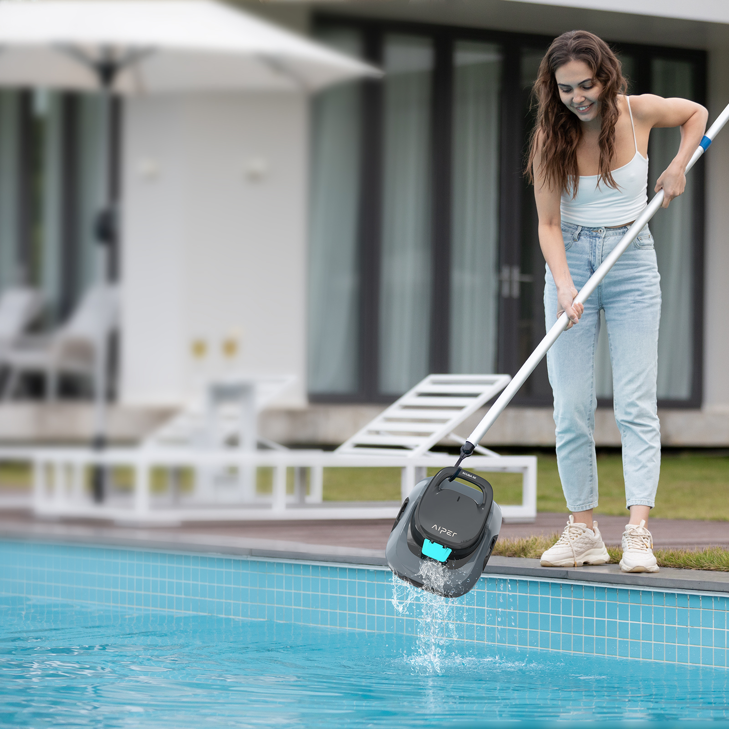 Woman using a pool cleaner, dipping it into water near an outdoor house and pool.