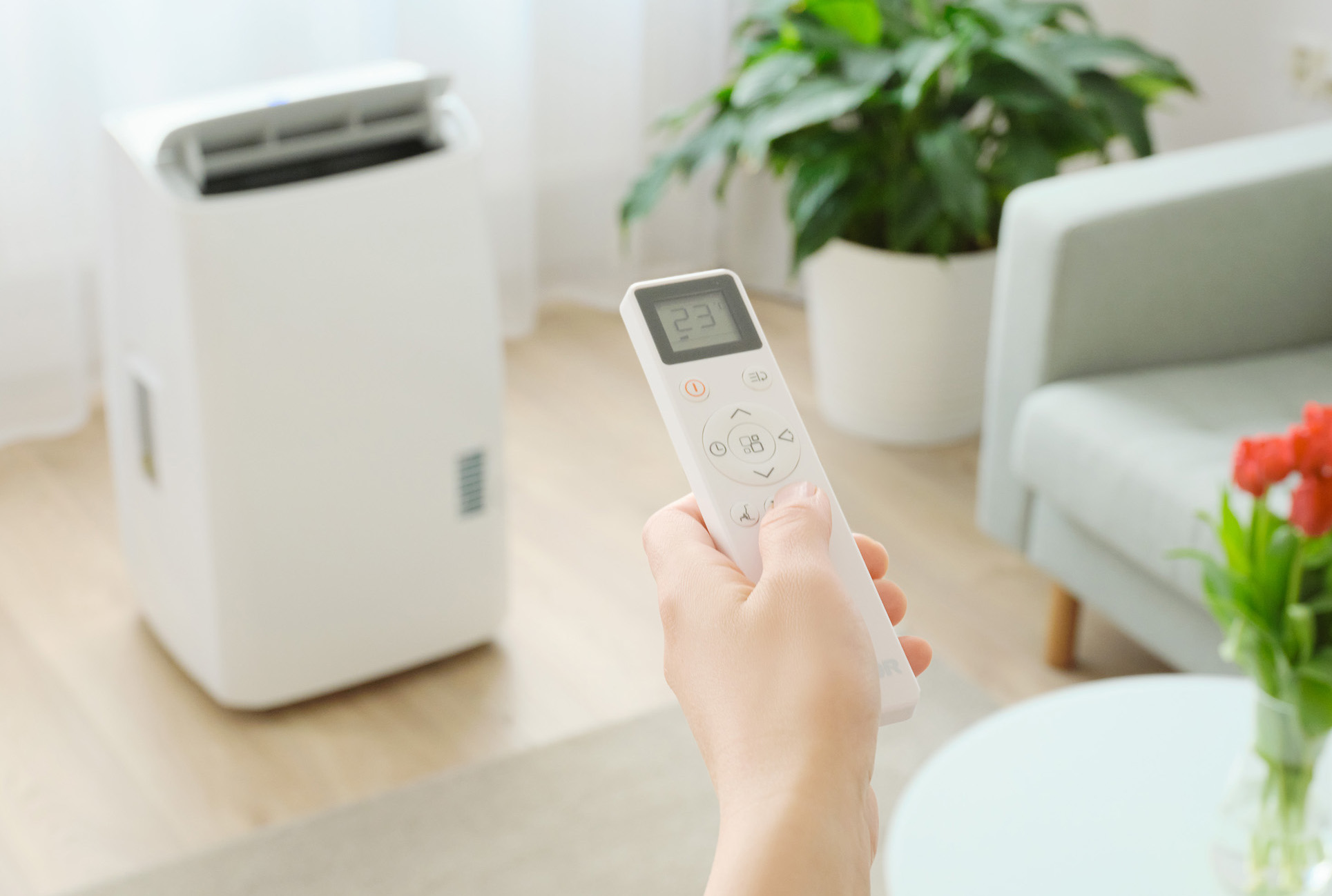 Dłoń trzymająca pilota, z białą klimatyzacją w tle.