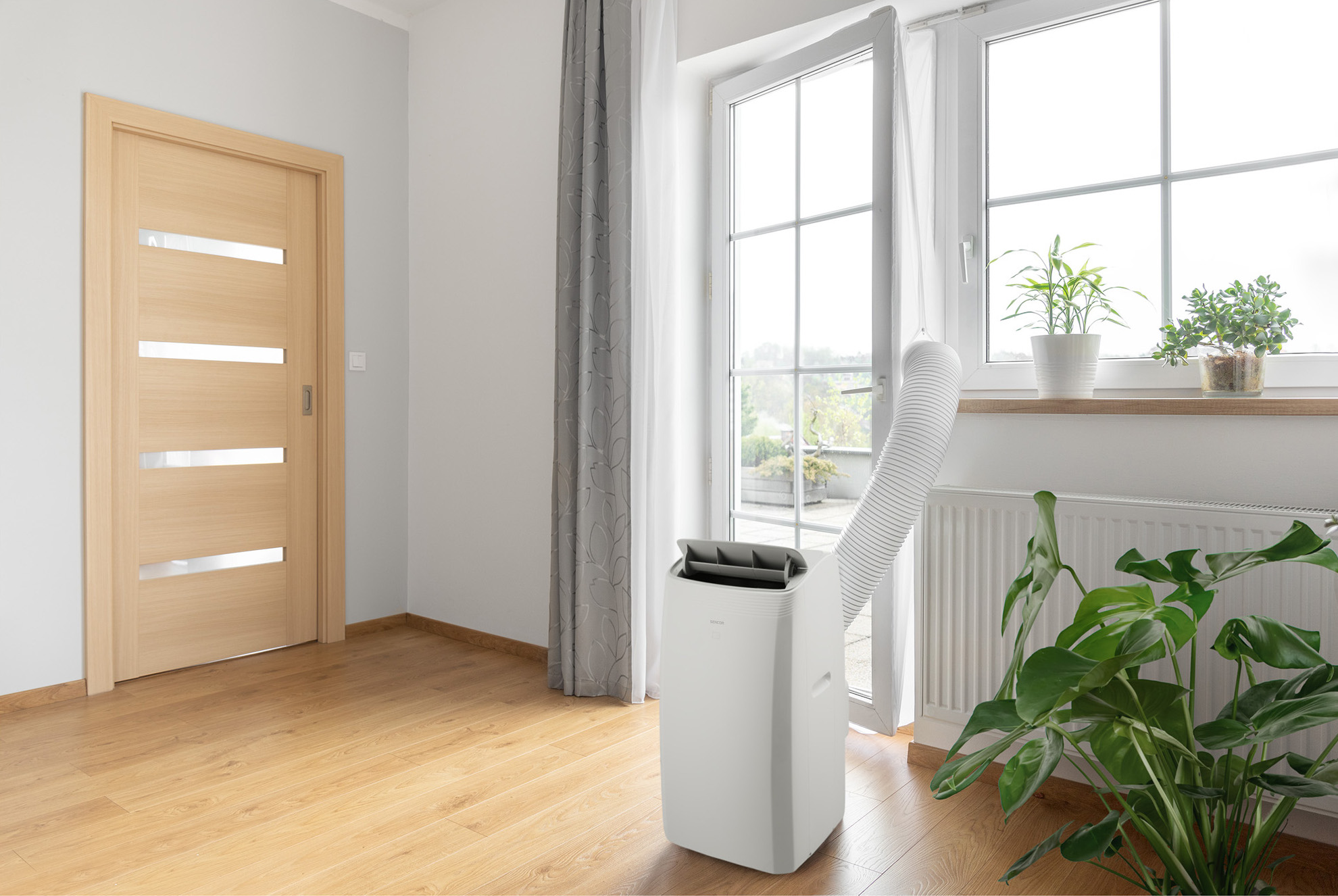 Białe przenośne urządzenie klimatyzacyjne w pokoju z oknem i drzwiami.