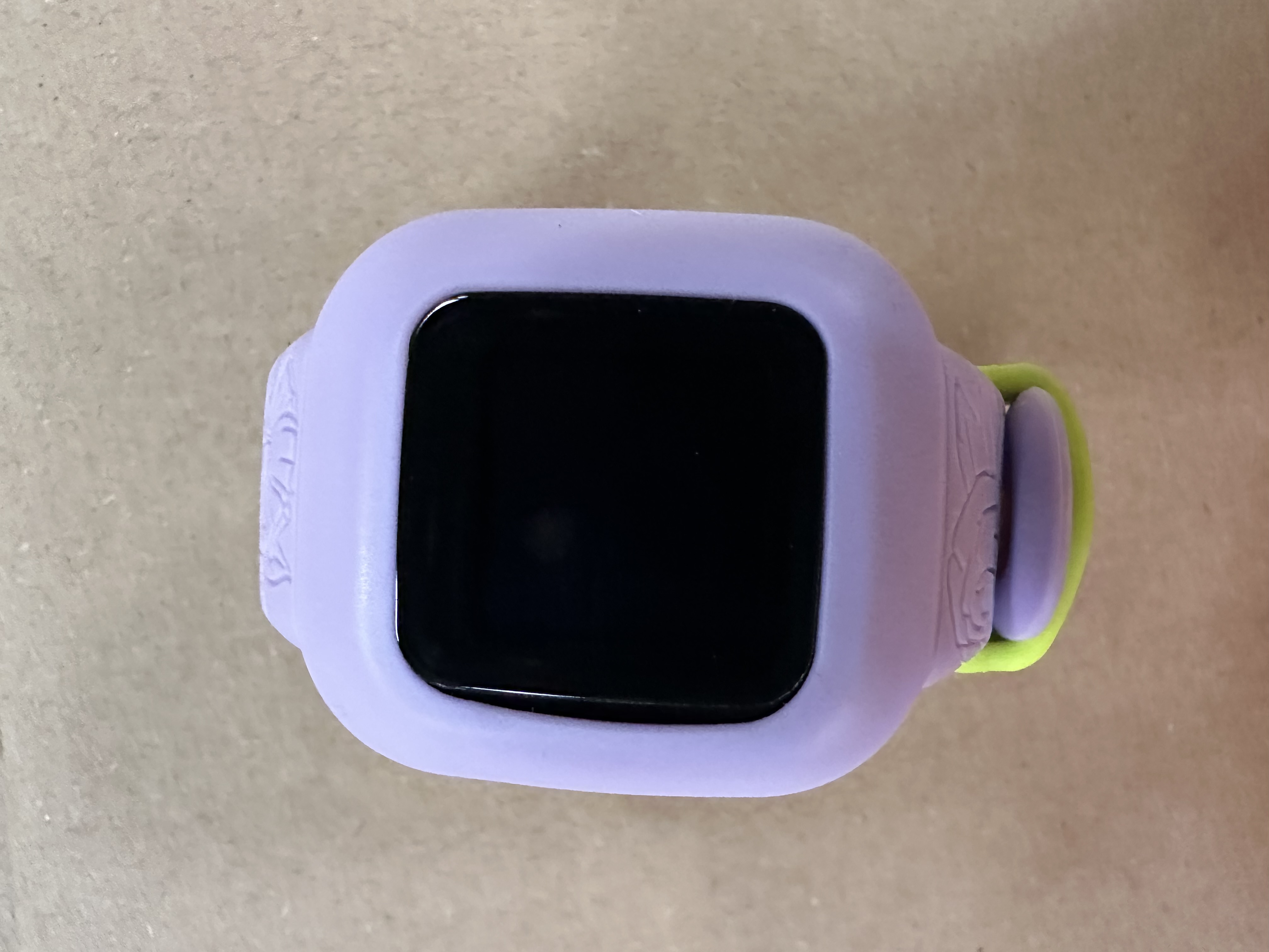 Smartwatch dla dziecka, fioletowy z czarnym ekranem. Pasek jest lawendowy z zielonym akcentem.