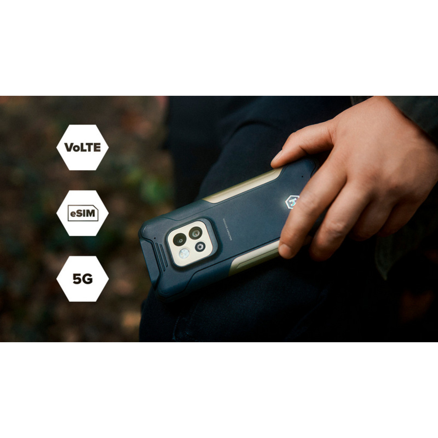 Een persoon houdt een zwarte smartphone met camera vast. De telefoon heeft de iconen VoLTE, eSIM en 5G. Achtergrond is wazige natuur.