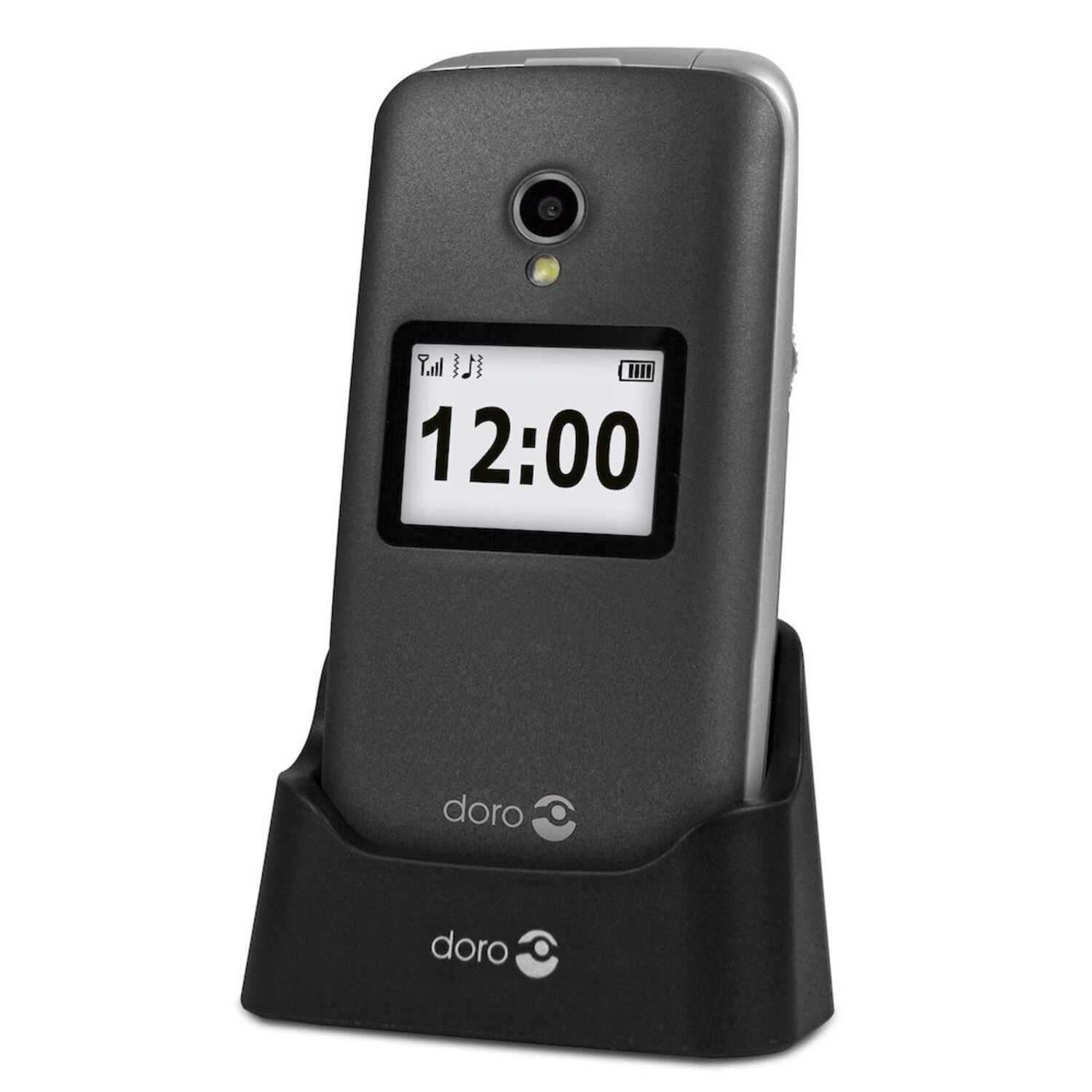 A closed silver flip phone in a black charging cradle. The screen displays the time: 12:00.