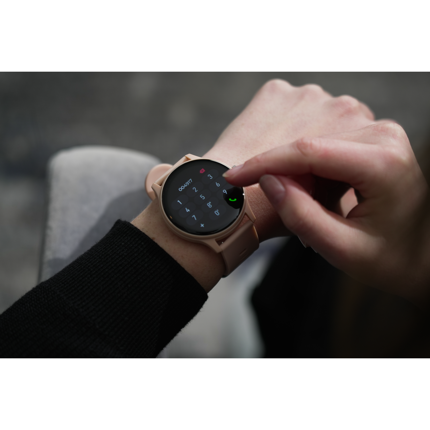 A person's hand interacts with a smartwatch, showing a dialing interface. Beige watch and band.