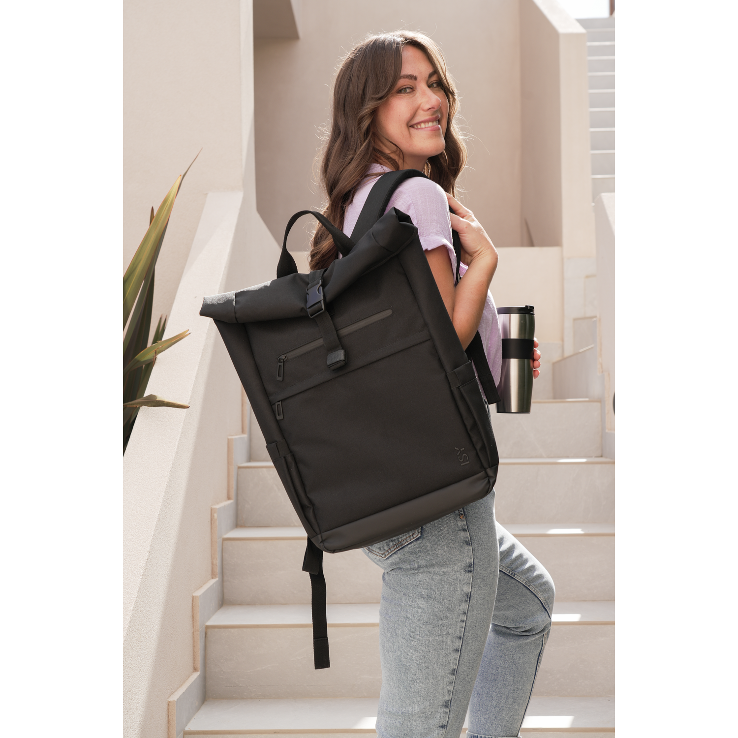 A woman with a black backpack and a thermos, walking up stairs.