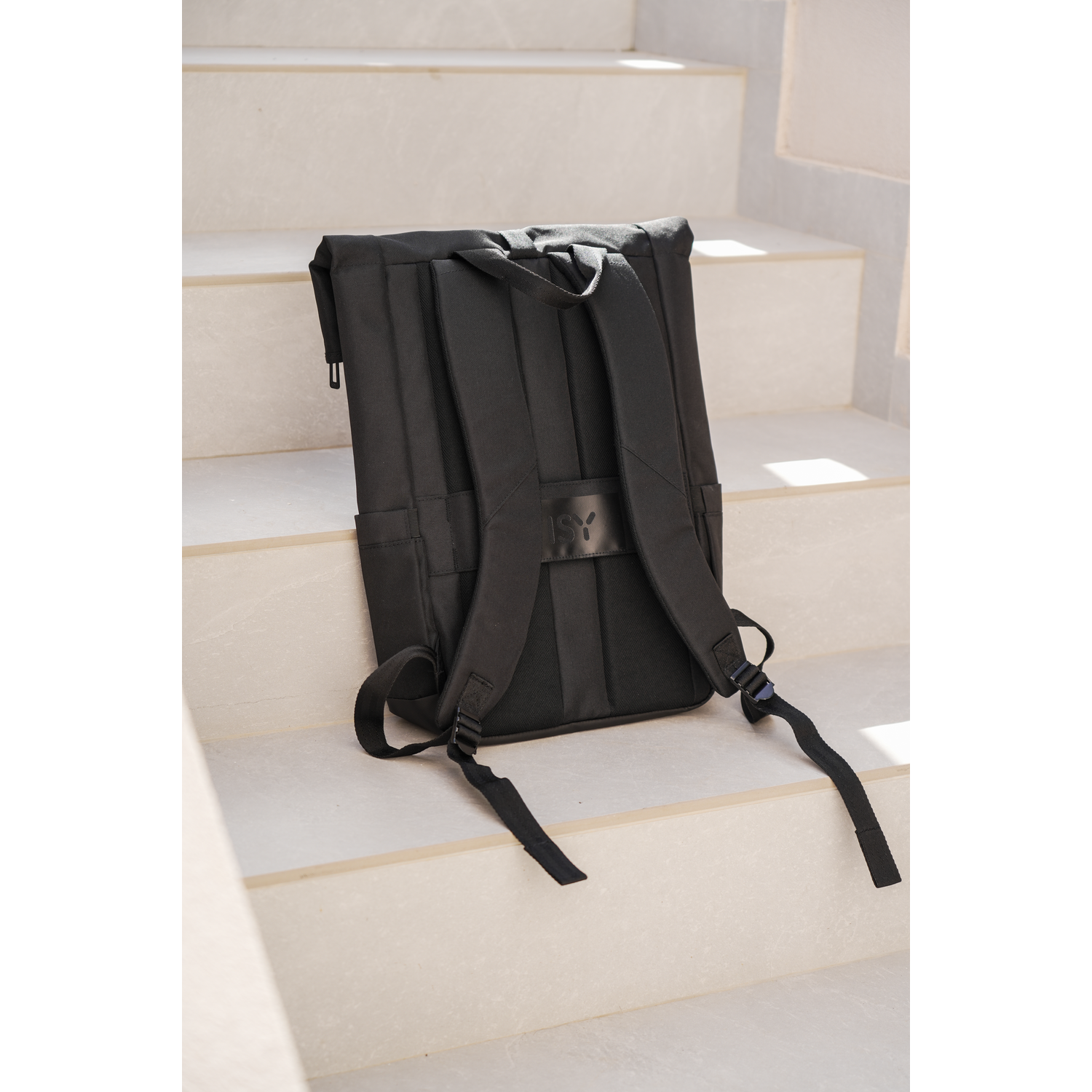 Black backpack on white stairs. The straps and back of the backpack are visible.