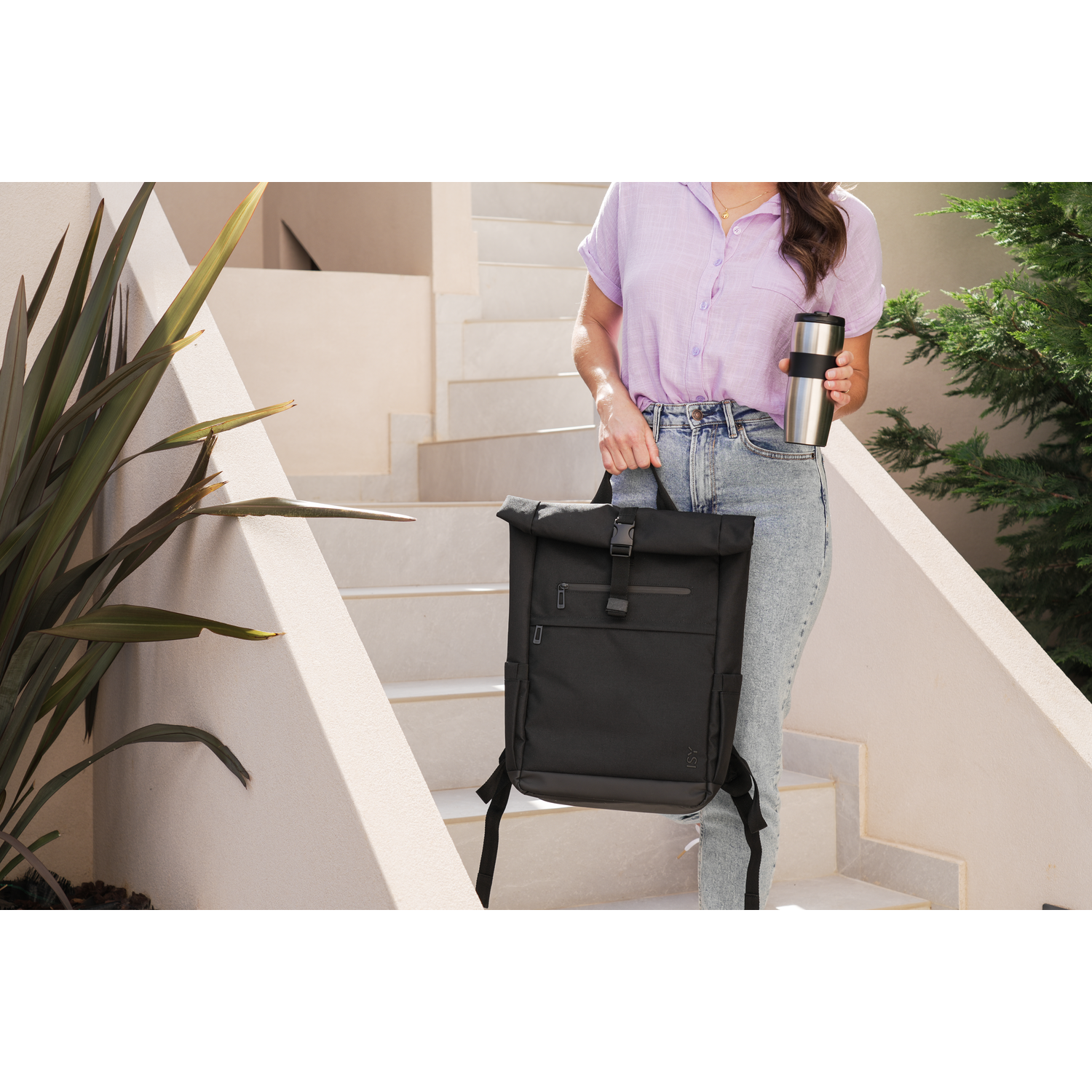 A person carrying a black backpack and a silver thermos walking up white stairs.